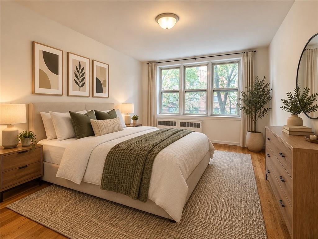 Staged bedroom with white bedding, olive-green accents, and a large window overlooking leafy trees.