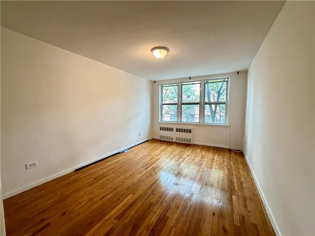Empty apartment room with hardwood floors and a wide window above a radiator.