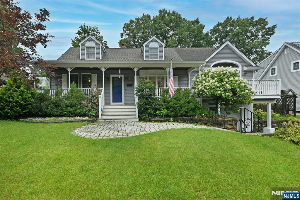 Gray home with a covered porch, blue front door, dormer windows, and a landscaped lawn.