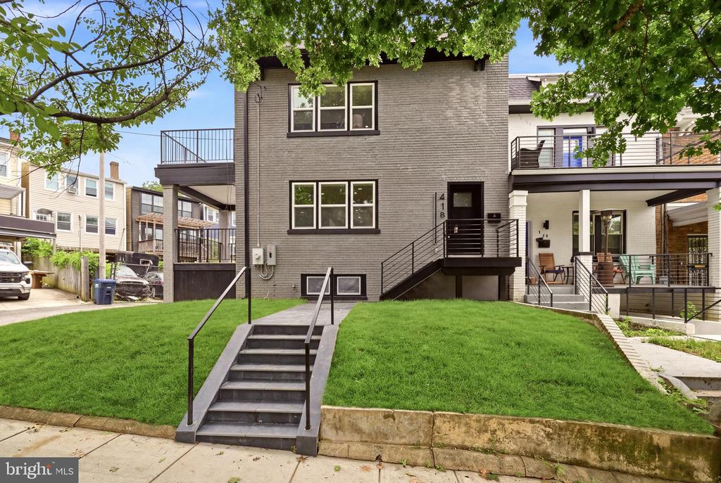 Gray brick home with a raised lawn, central entry stairs, and covered porches and balconies.