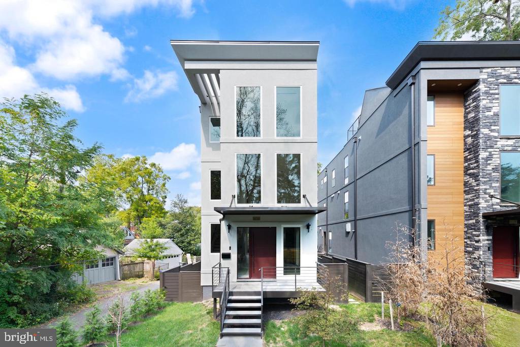 Modern white multi-story home with a raised front entrance and steps, flanked by contemporary townhouses.