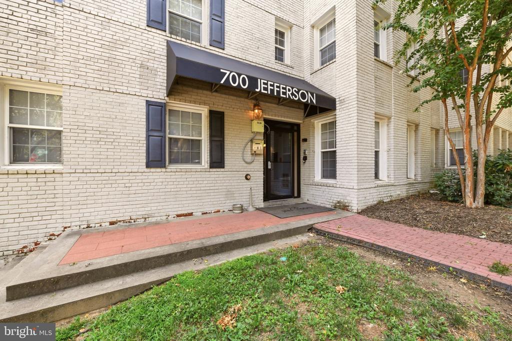White brick apartment entrance beneath a black 700 Jefferson awning, with a raised red-tiled walkway and steps.