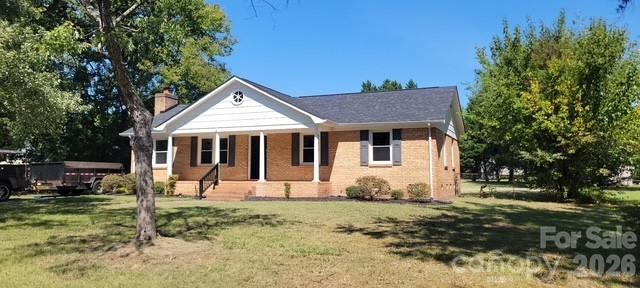 Single-story brick house with a white covered porch, broad lawn, and mature trees.