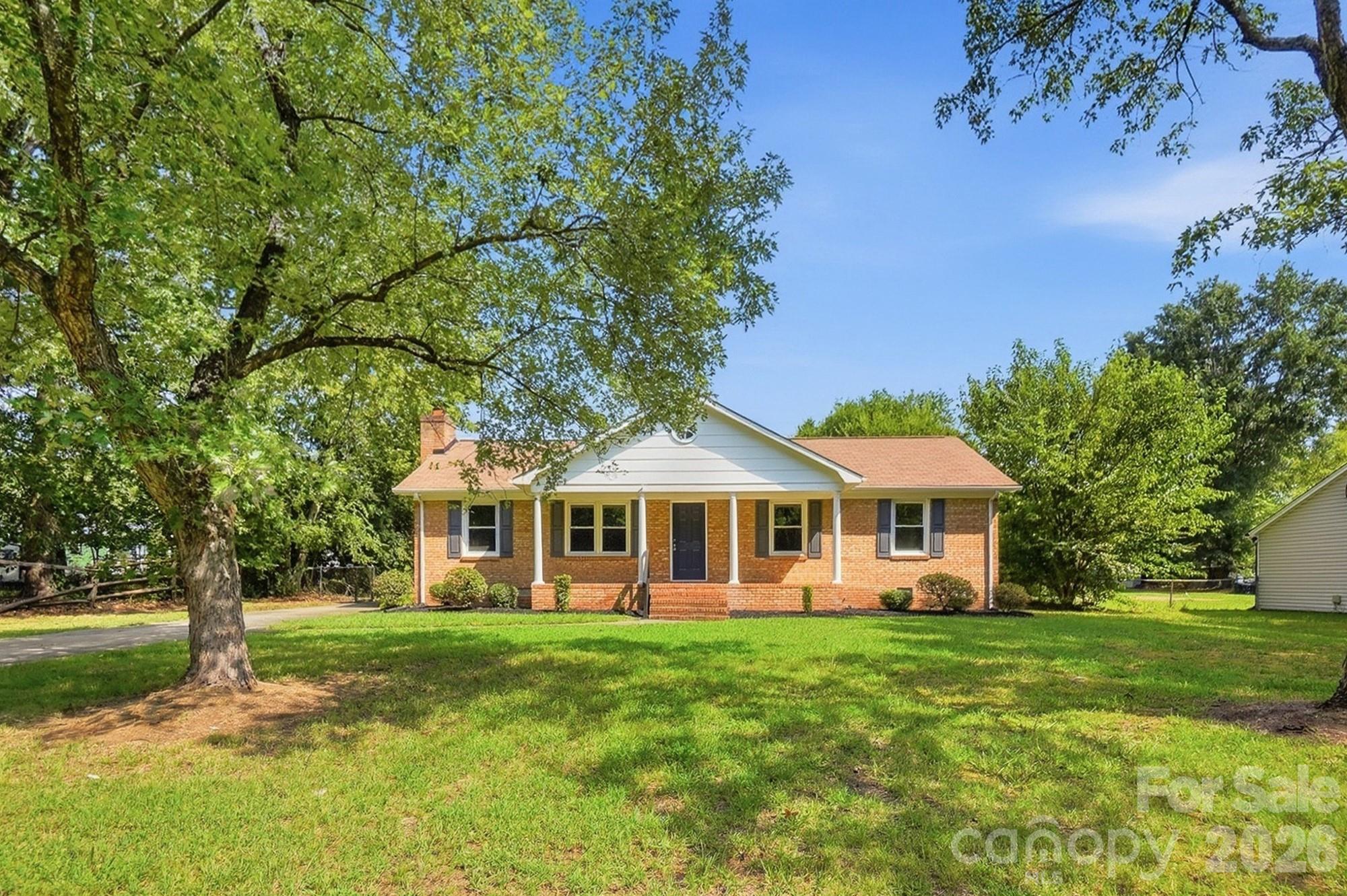 Brick ranch house with a white front porch, broad lawn, and large shade tree.