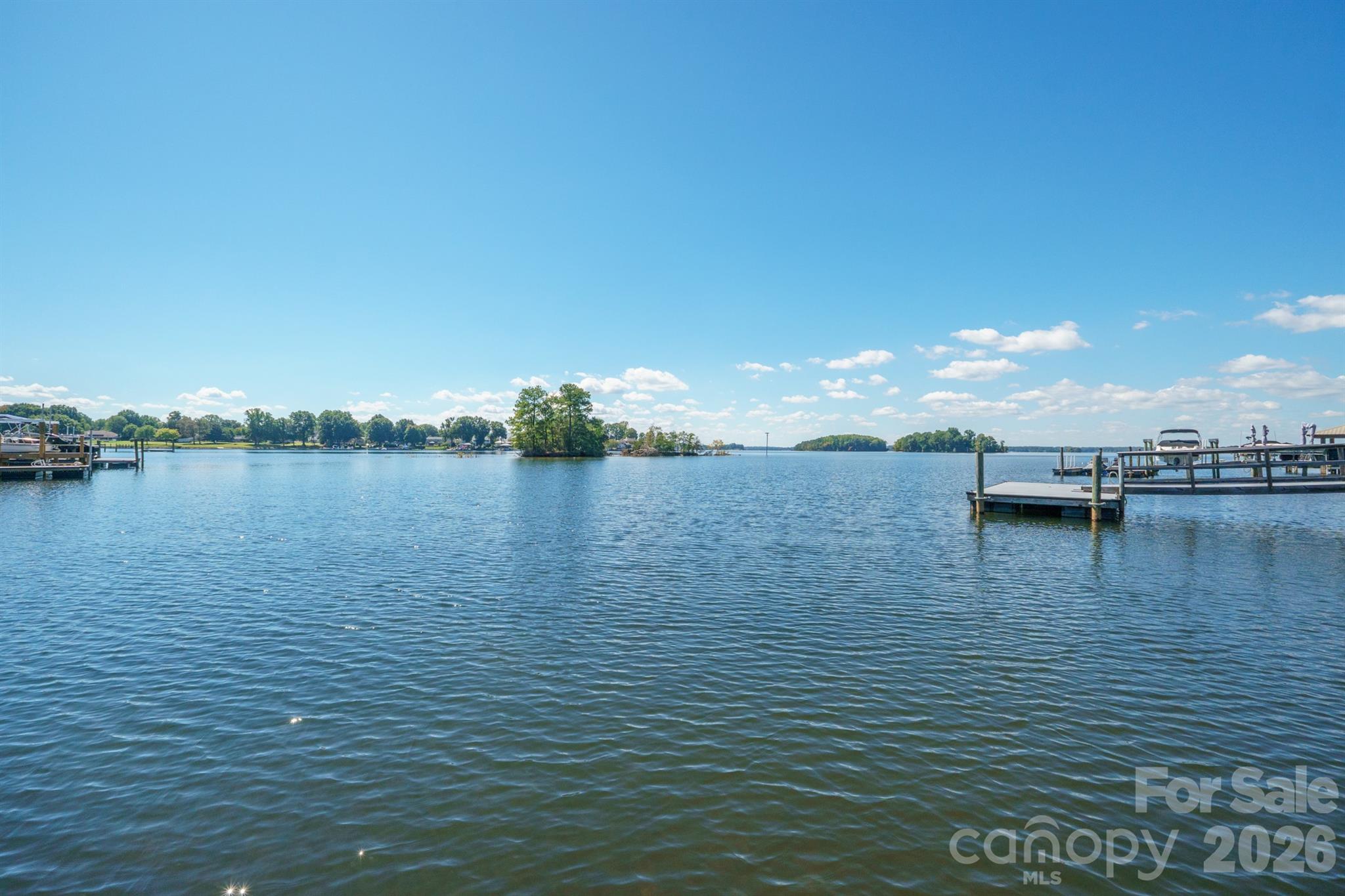 Lake waterfront with boat docks and a small tree-covered island under a blue sky.