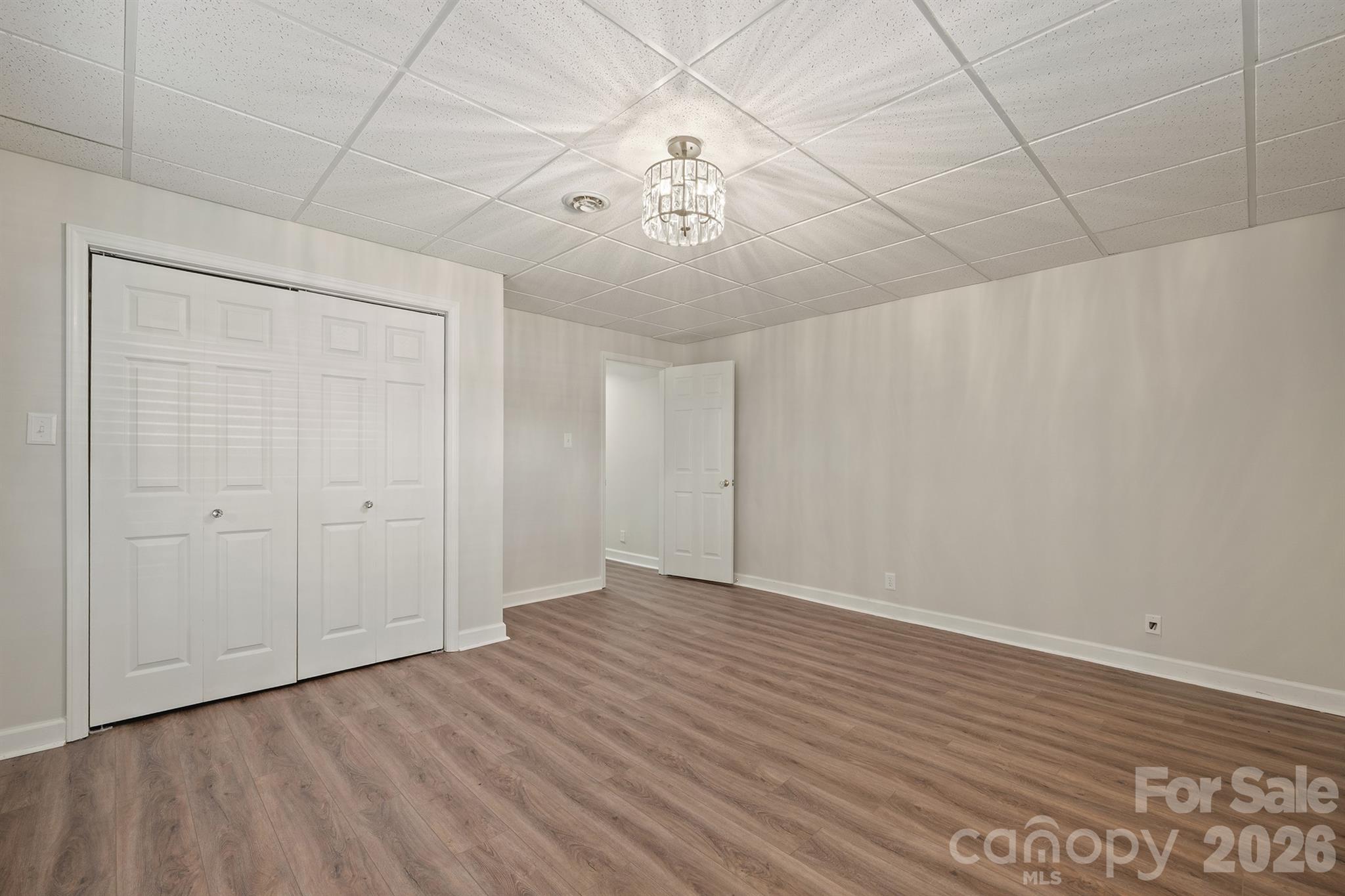 Empty room with brown wood-look flooring, white closet doors, and a ceiling light.