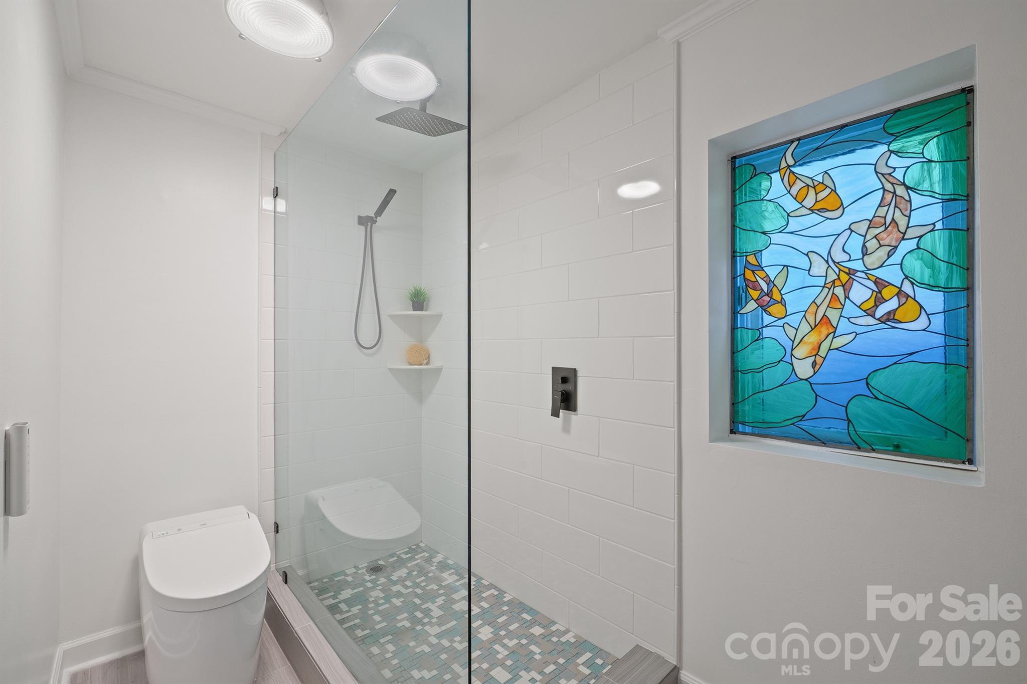 Modern bathroom with a glass walk-in shower and colorful stained-glass fish window.