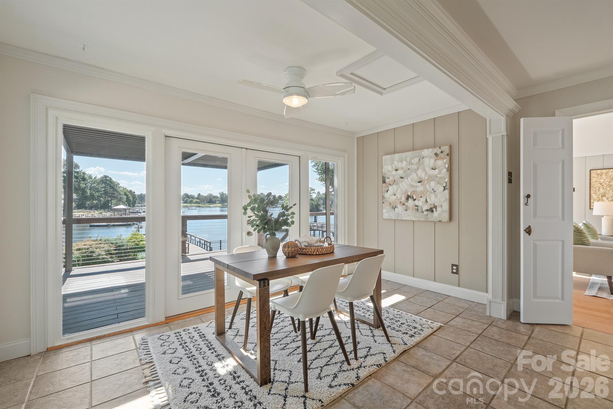 Dining area with lake views through glass doors, a wood table, and white chairs.