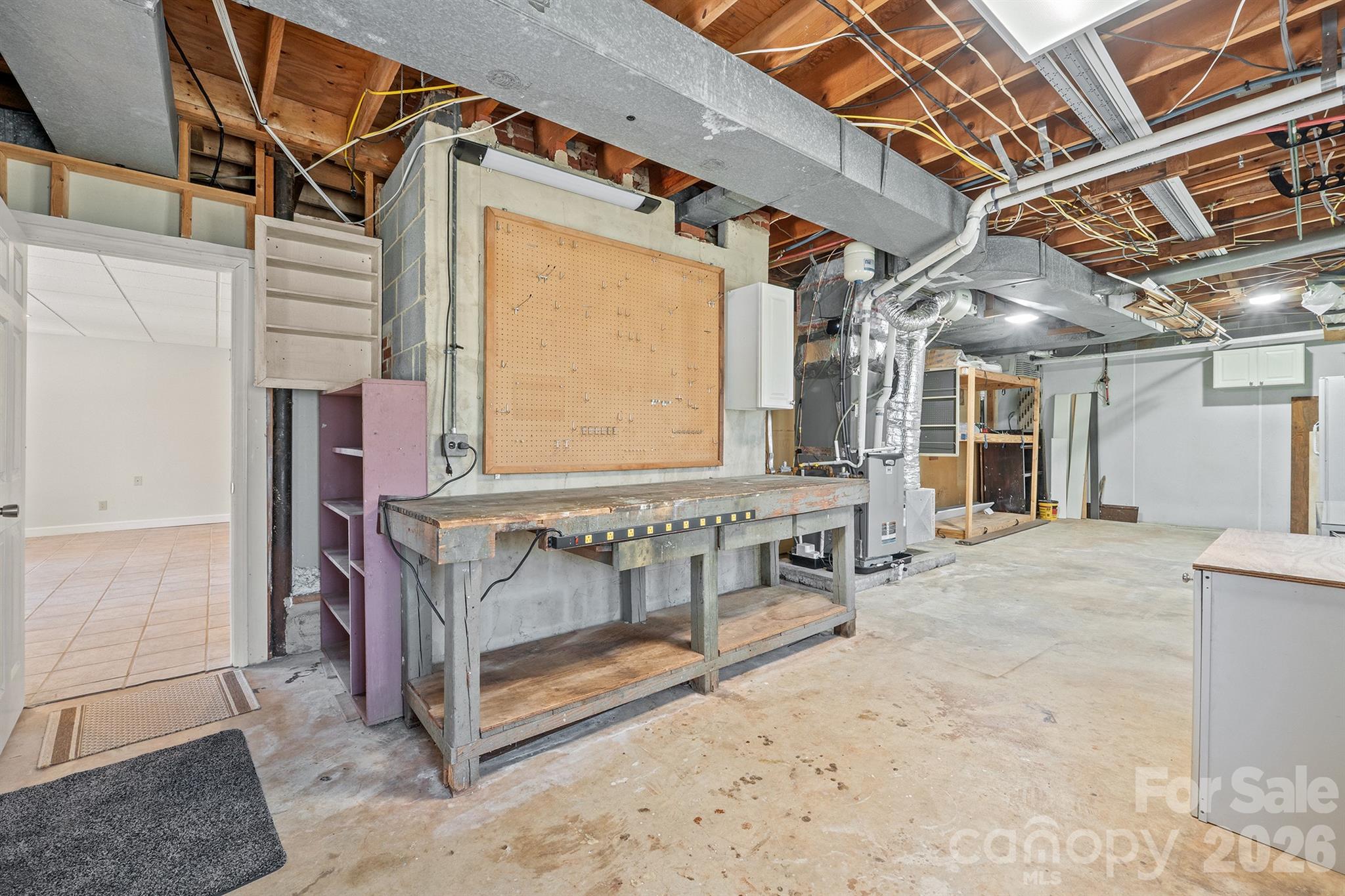 Basement workshop with a large workbench, pegboard tool wall, and exposed ceiling joists and ductwork.