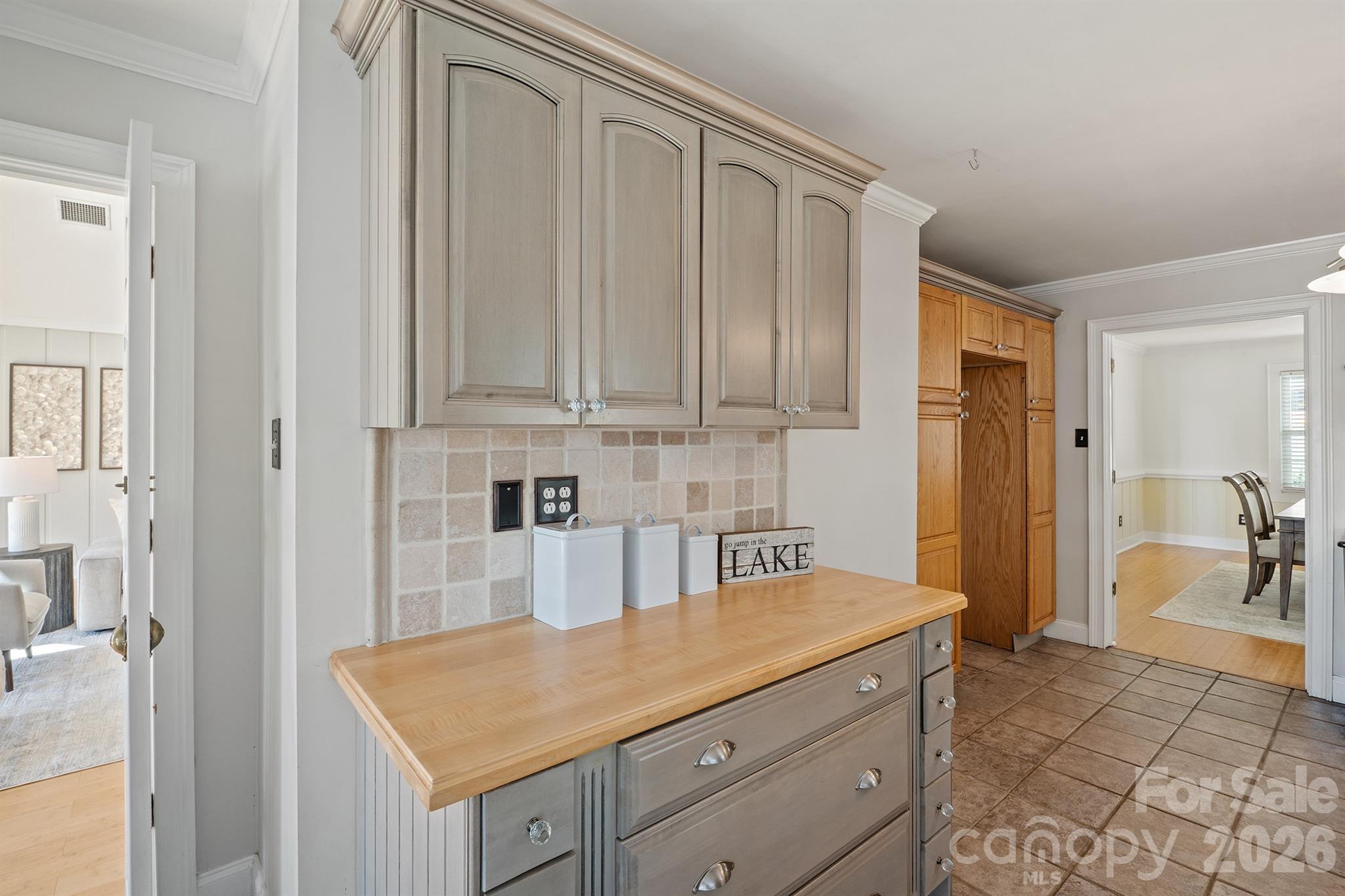 Kitchen counter with gray cabinets, a light wood worktop, and tiled backsplash.