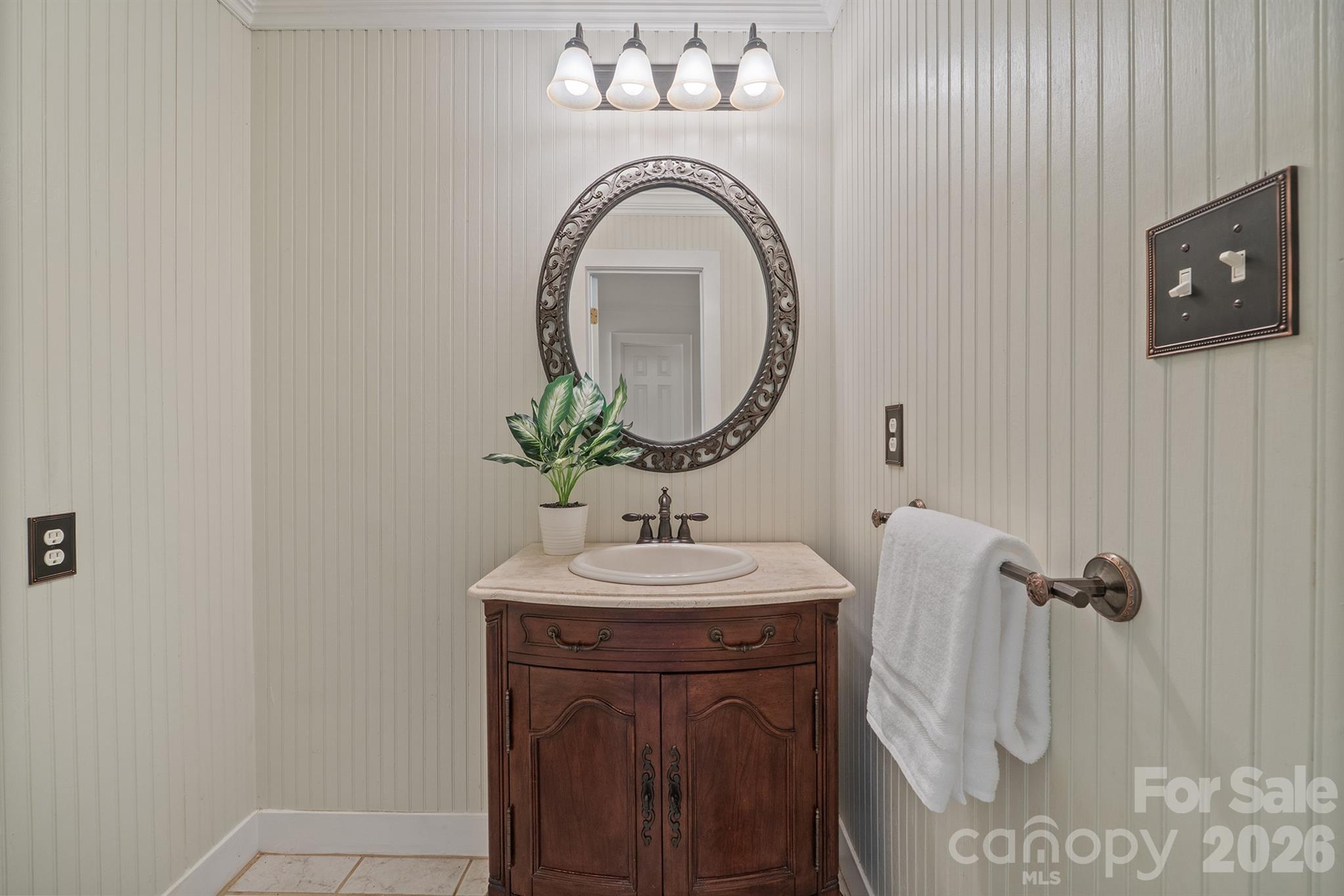 Bathroom vanity with a dark wood cabinet, ornate round mirror, and white paneled walls.