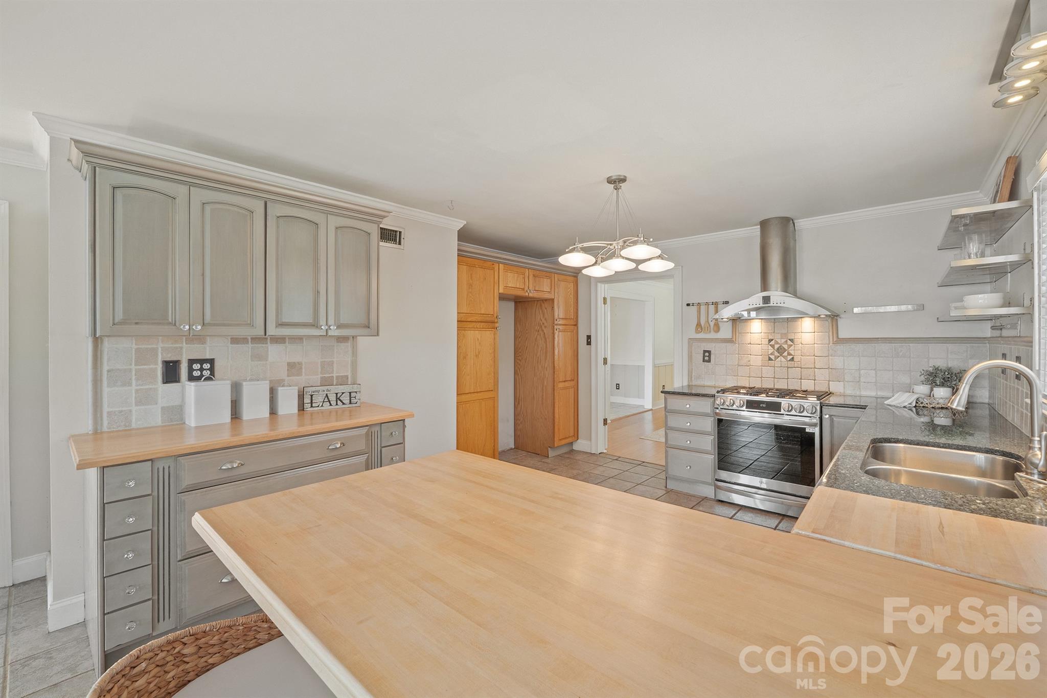 Kitchen with gray cabinets, a stainless steel range, and a large light-wood island.