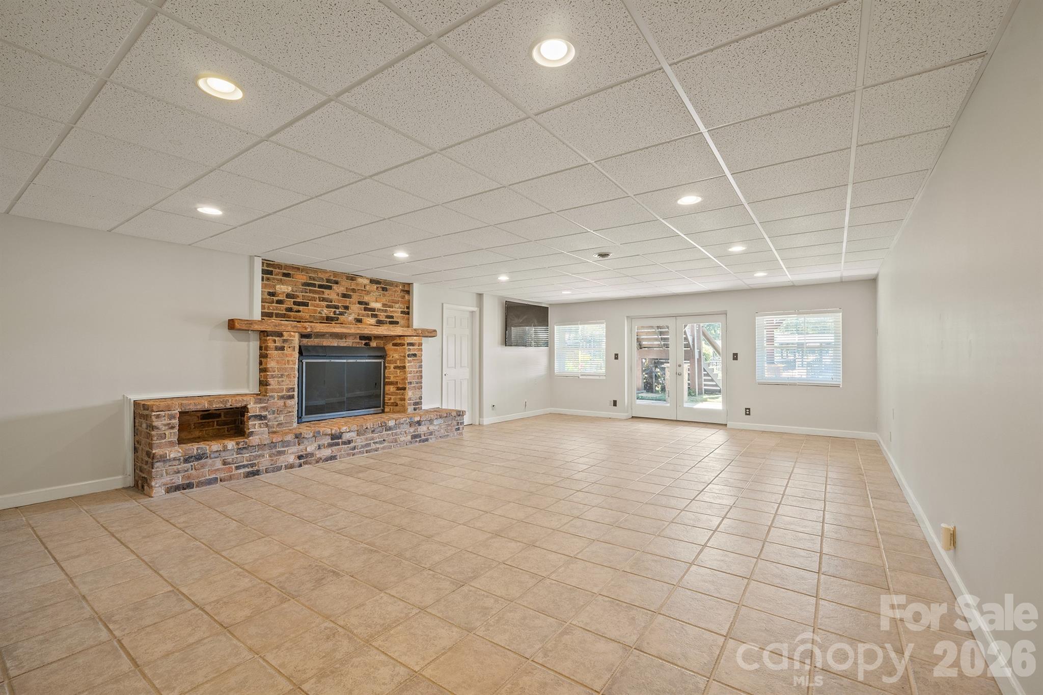 Empty tiled room with a brick fireplace and glass doors to the outdoors.