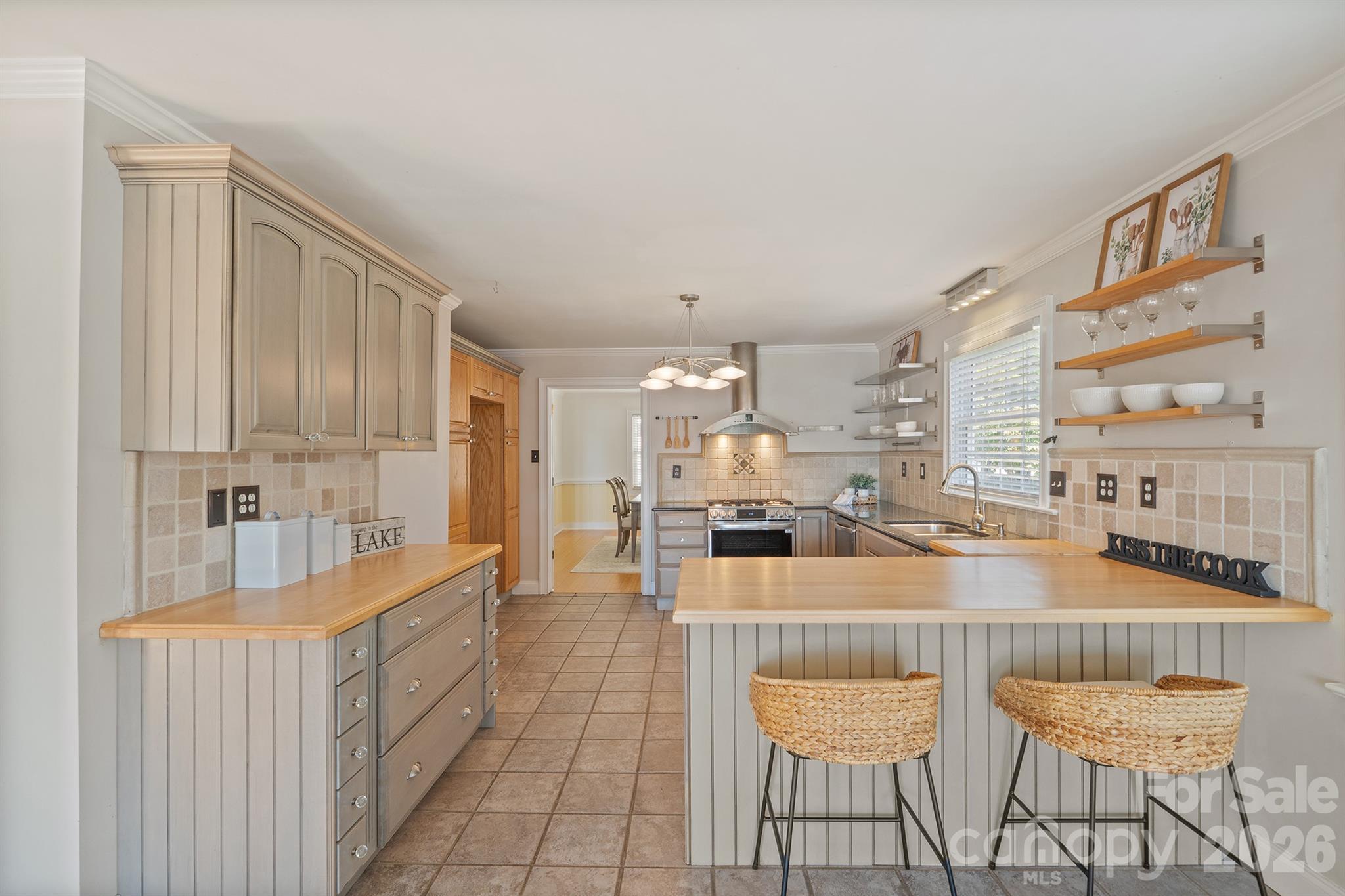 Kitchen with a wood-topped island, woven stools, gray cabinetry, and stainless-steel range.