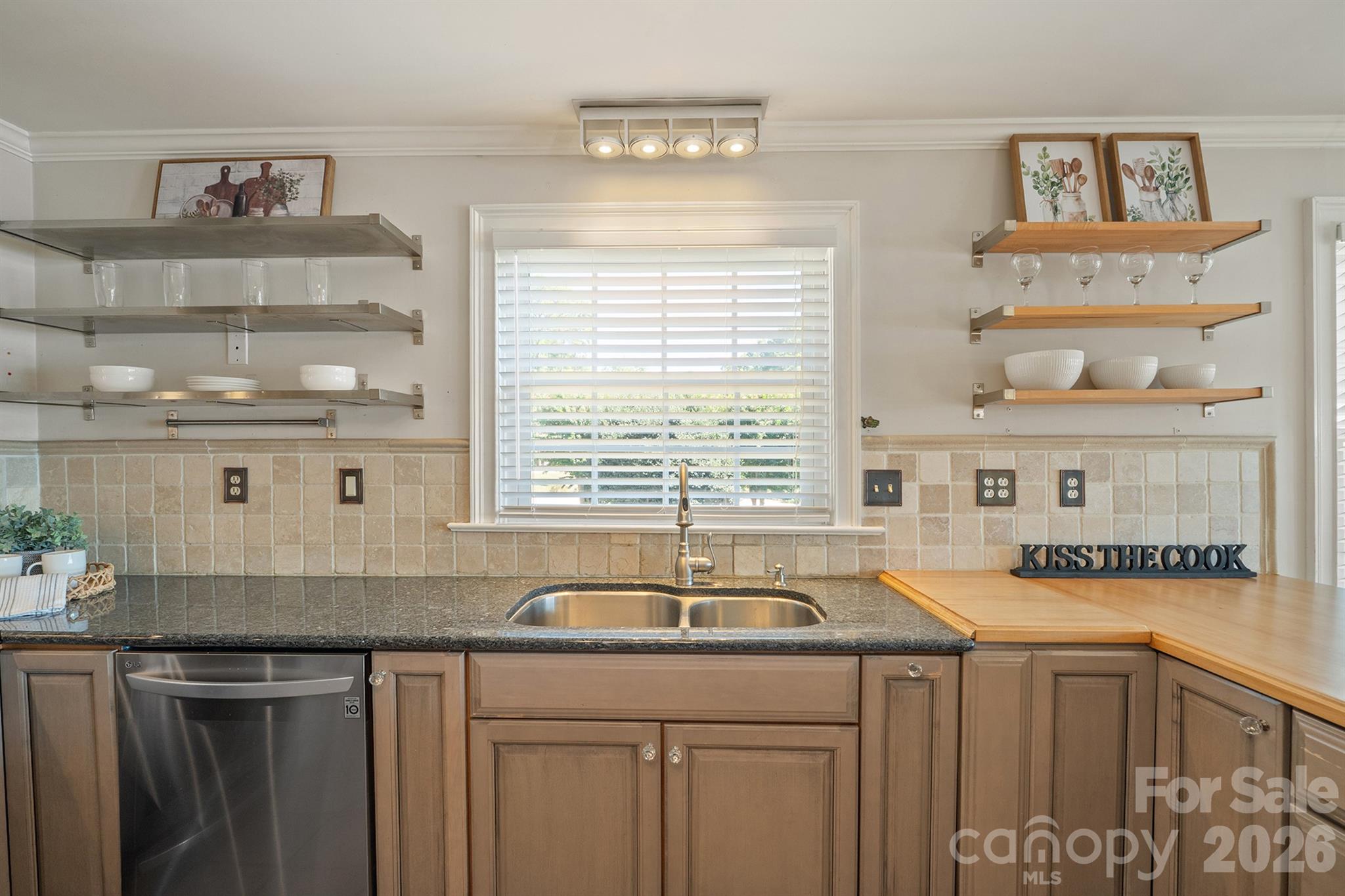 Kitchen with warm wood cabinets, granite counters, open shelves, and a double sink beneath a window.