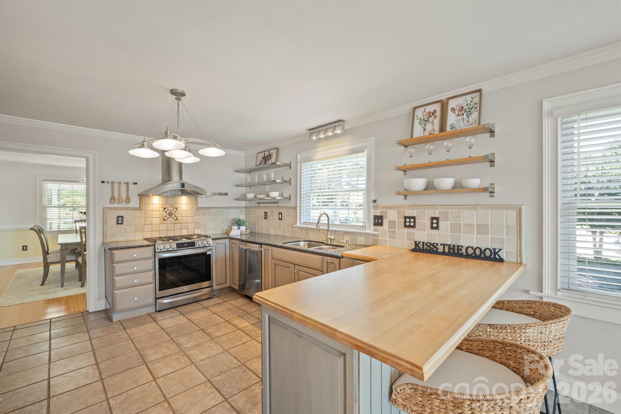 Kitchen with a stainless-steel range, tiled backsplash, open shelves, and a large butcher-block breakfast bar.