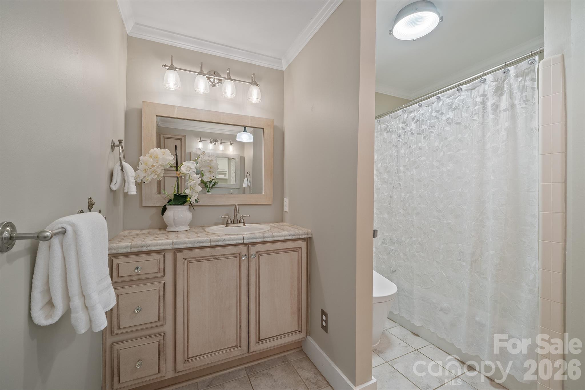 Bathroom with a light wood vanity and sink beside a white patterned shower curtain.