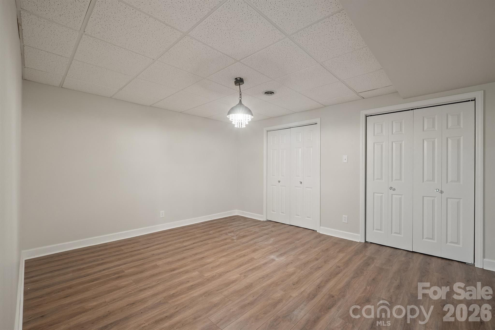 Empty room with wood-look flooring, two sets of white closet doors, and a crystal pendant light.