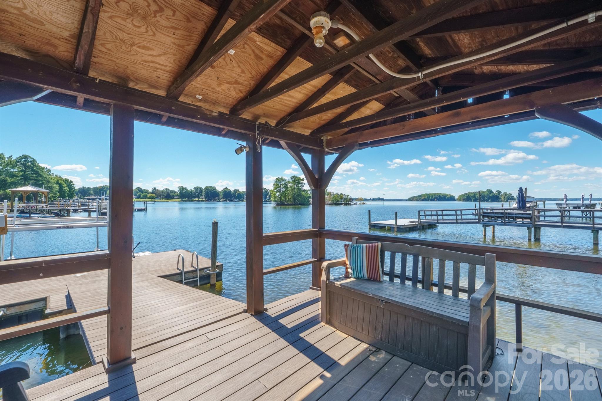 Covered lakeside dock with a wooden deck and bench overlooking the water and boat slips.