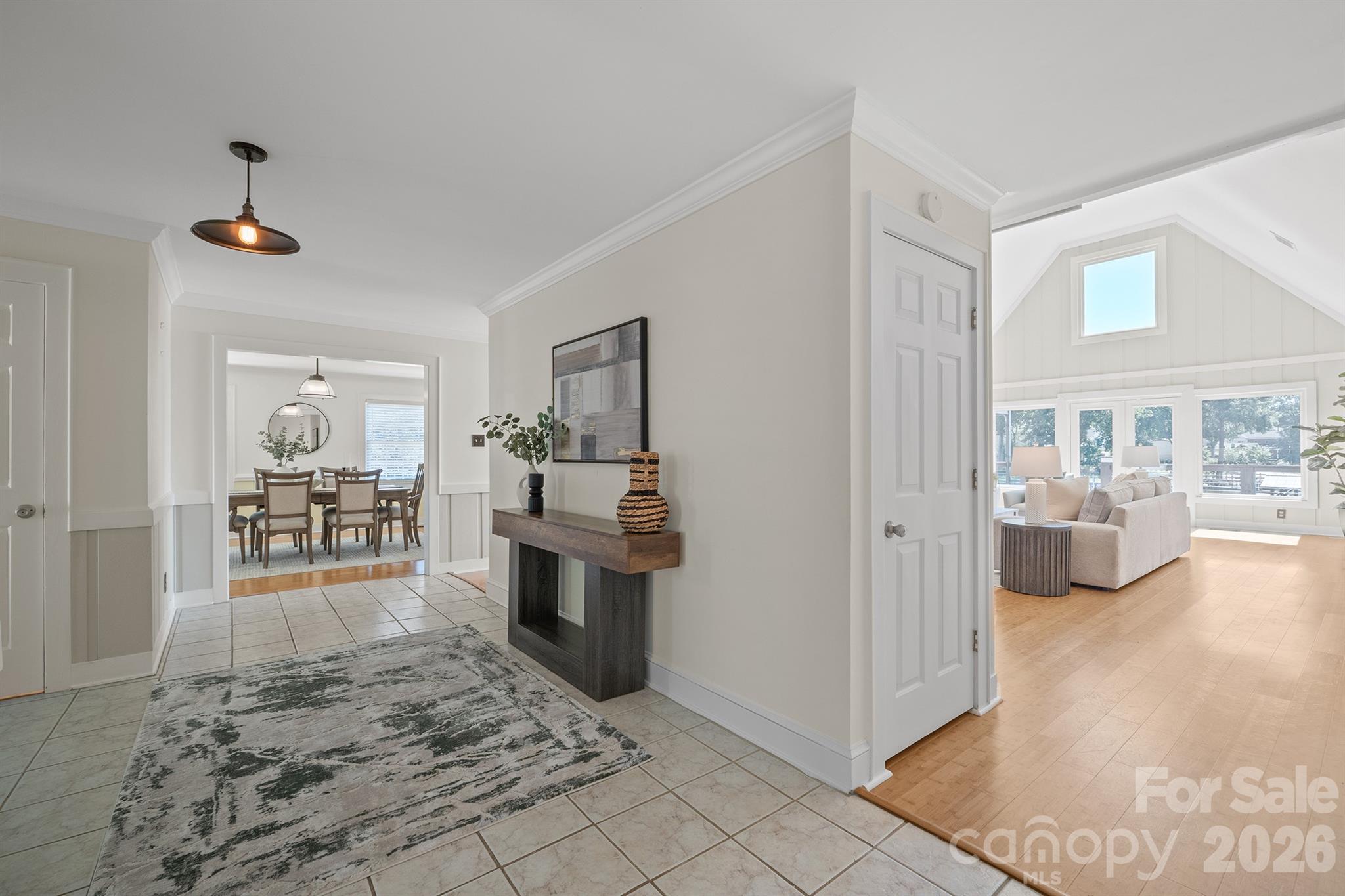 Staged entry foyer with tiled floors, opening to a dining room and a sunlit vaulted living room.