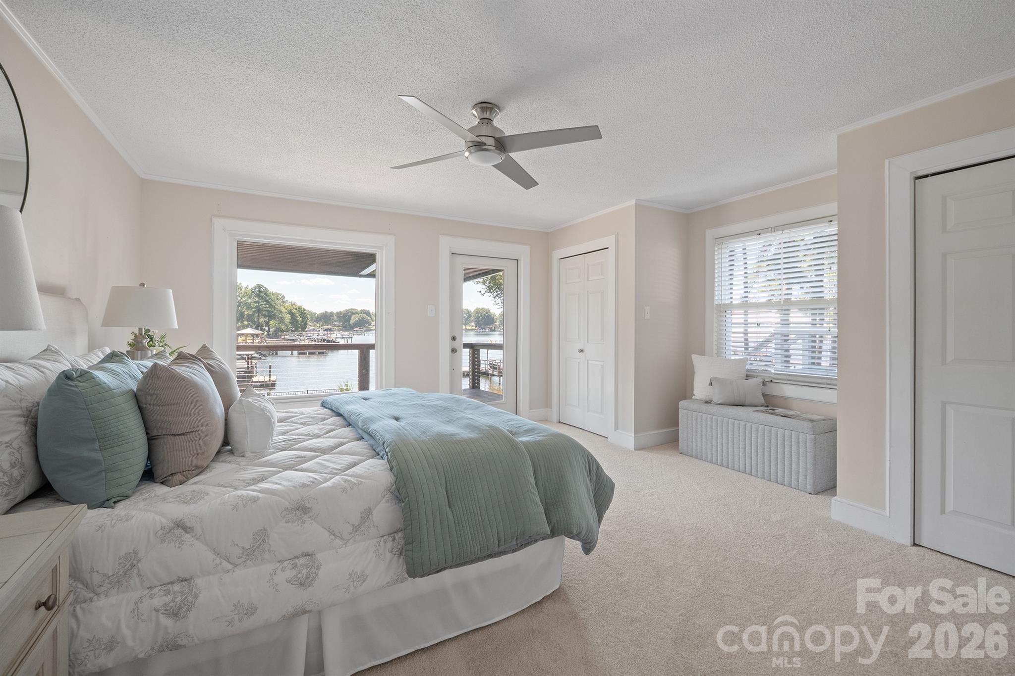 Bedroom with blue-gray bedding and a water view through the window and glass door.