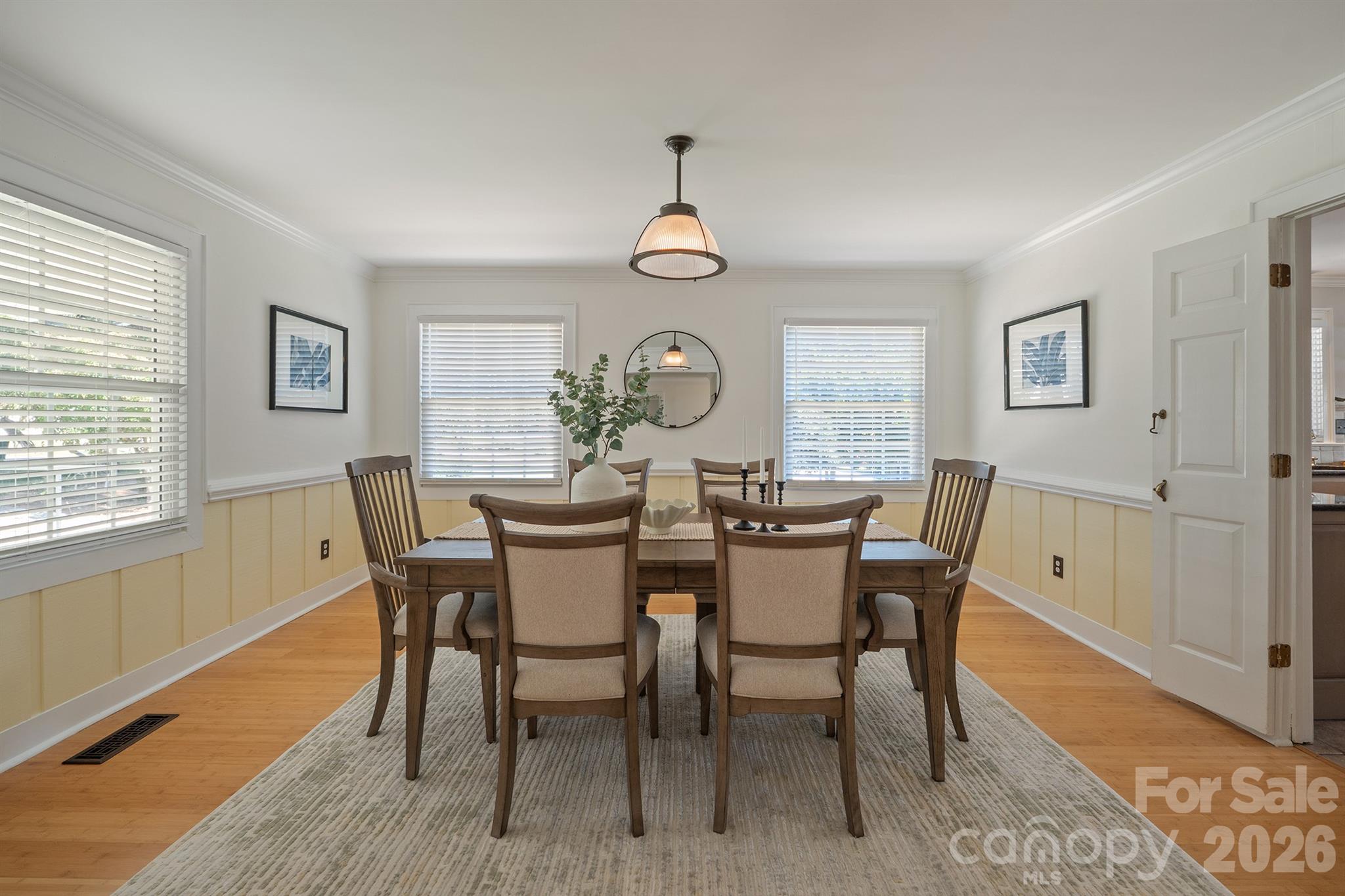 Dining room with a wooden table and upholstered chairs, yellow wainscoting, and hardwood floors.