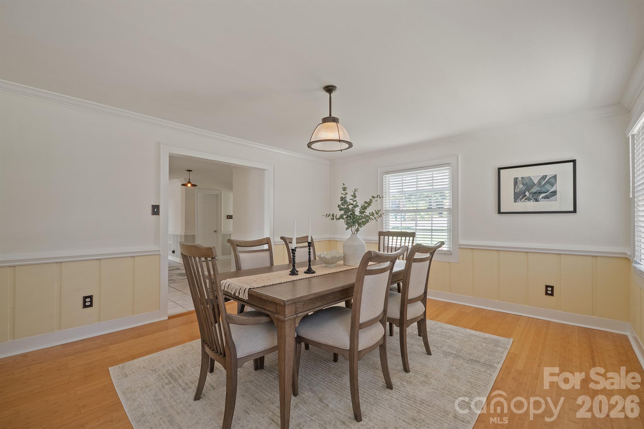 Dining room with a wooden table, upholstered chairs, pale yellow wainscoting, and hardwood floors.