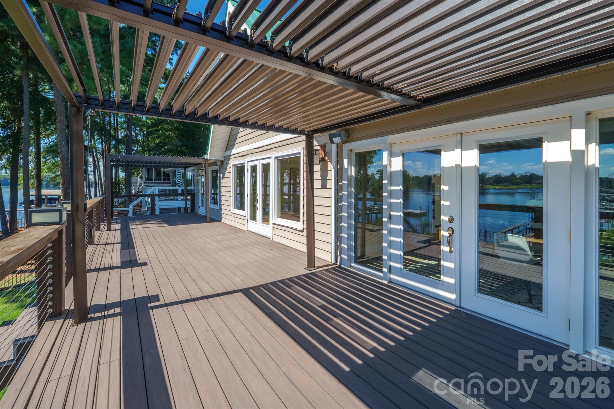 Lakeside home deck beneath a slatted pergola, with glass doors and views over the water.