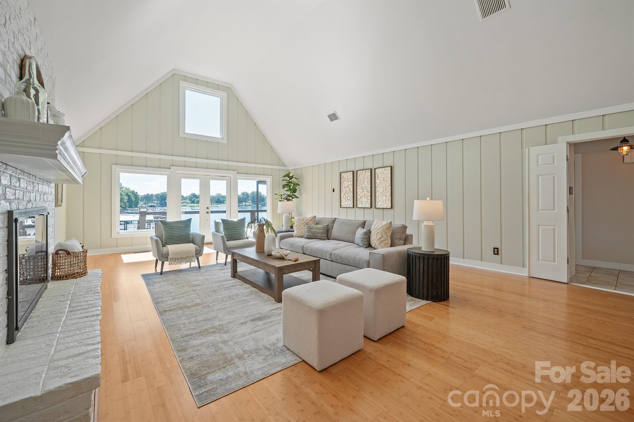 Staged living room with vaulted ceiling, white brick fireplace, and lake views through large windows.