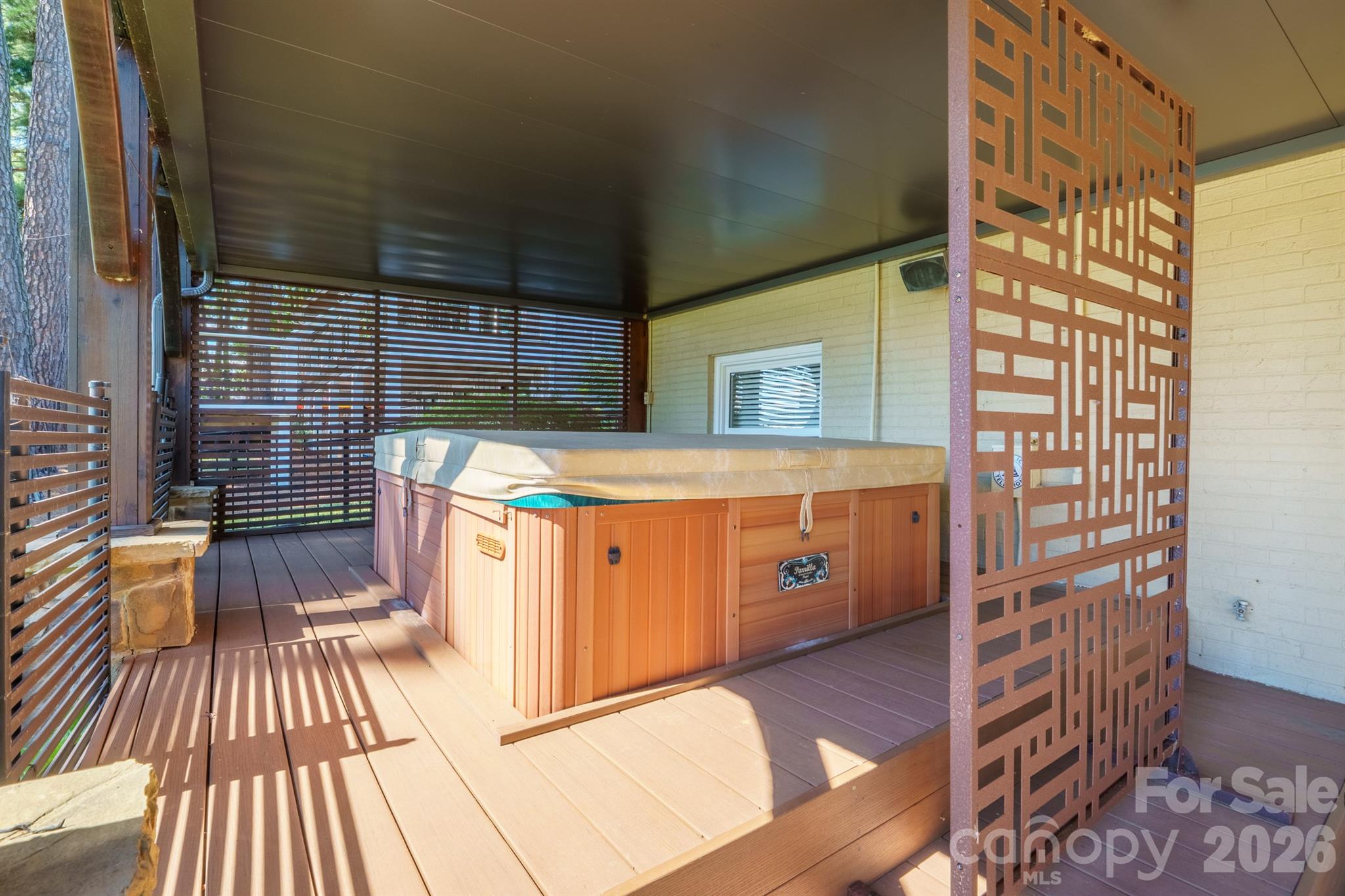 Covered deck with a large hot tub and slatted wood privacy screens.