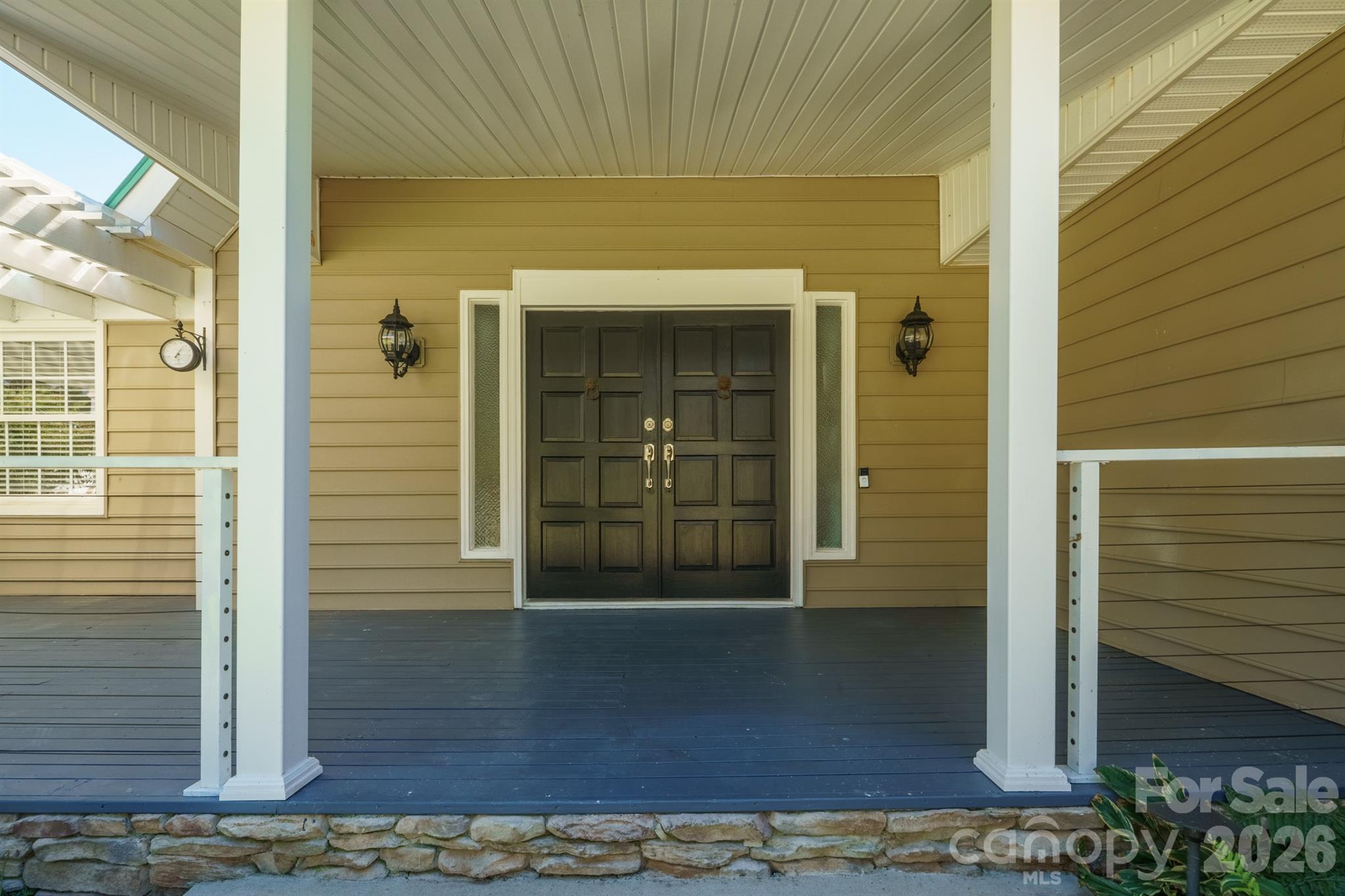 Covered front porch with dark double doors, white columns, tan siding, and a stone foundation.