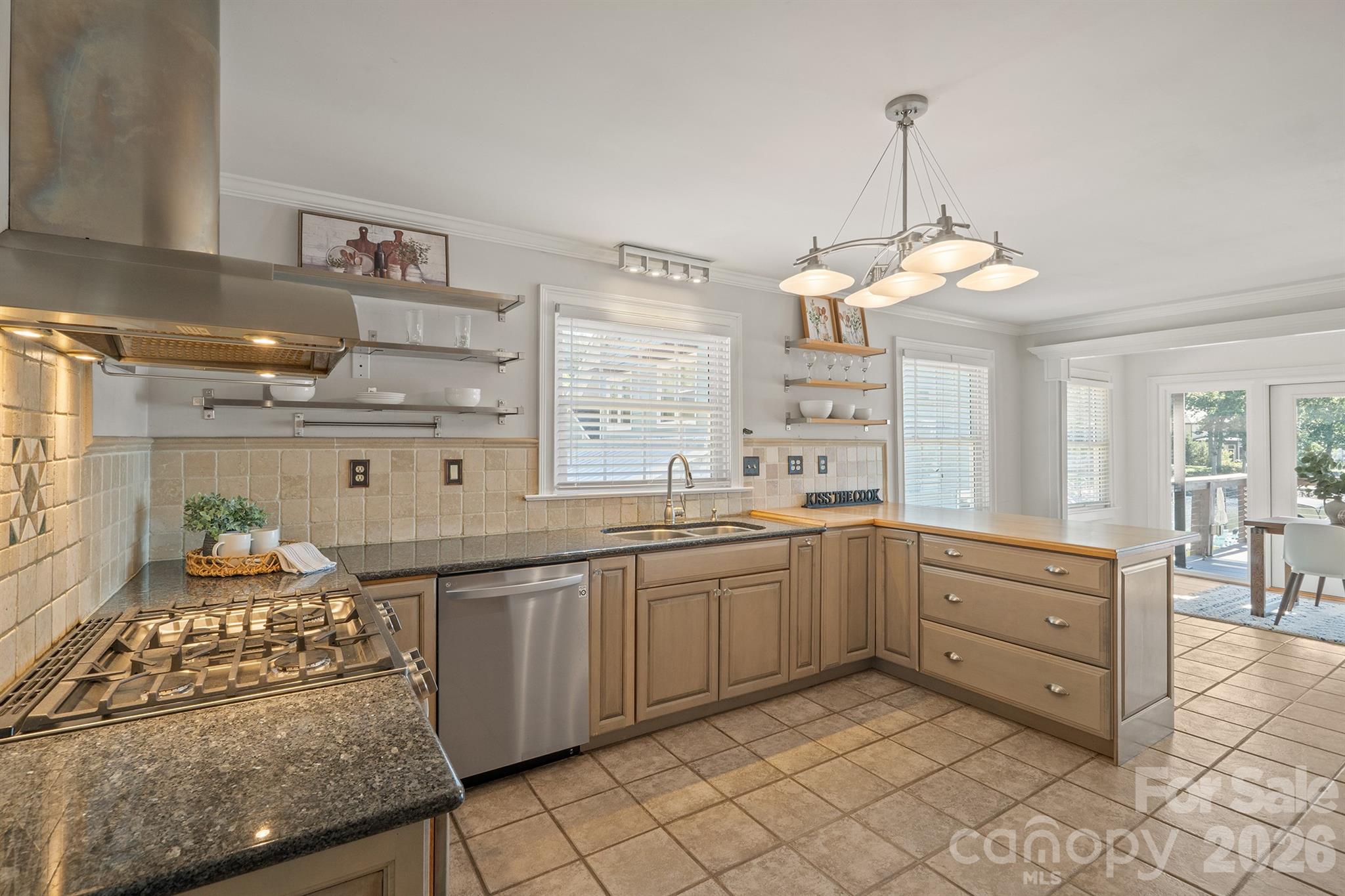 Bright kitchen with granite counters, a gas range, stainless appliances, and a wood island beside the dining area.