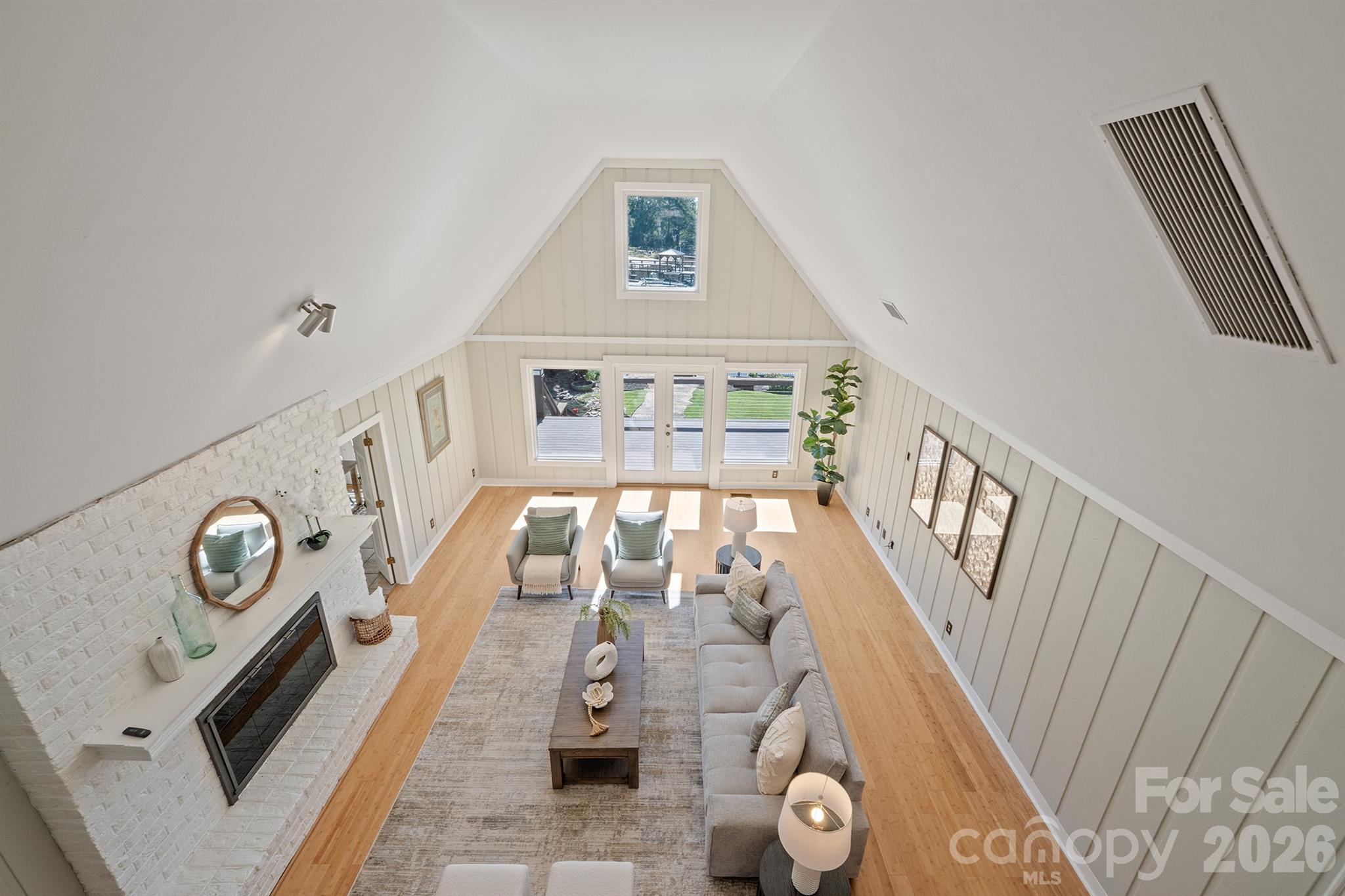 Vaulted living room with a white brick fireplace, light wood floors, and glass doors to the yard.