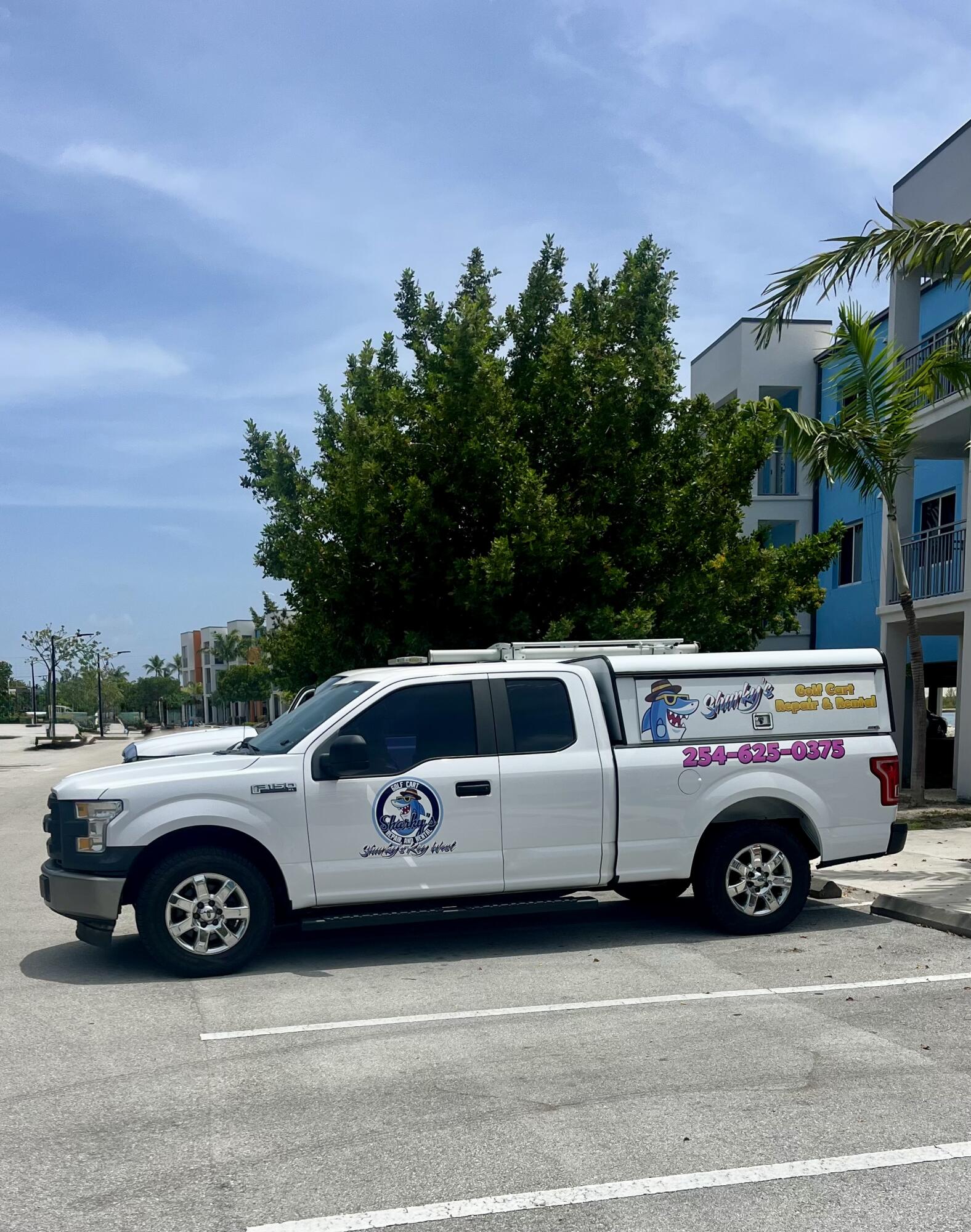 White Sharky's golf cart repair and rental pickup truck parked beside a modern building.