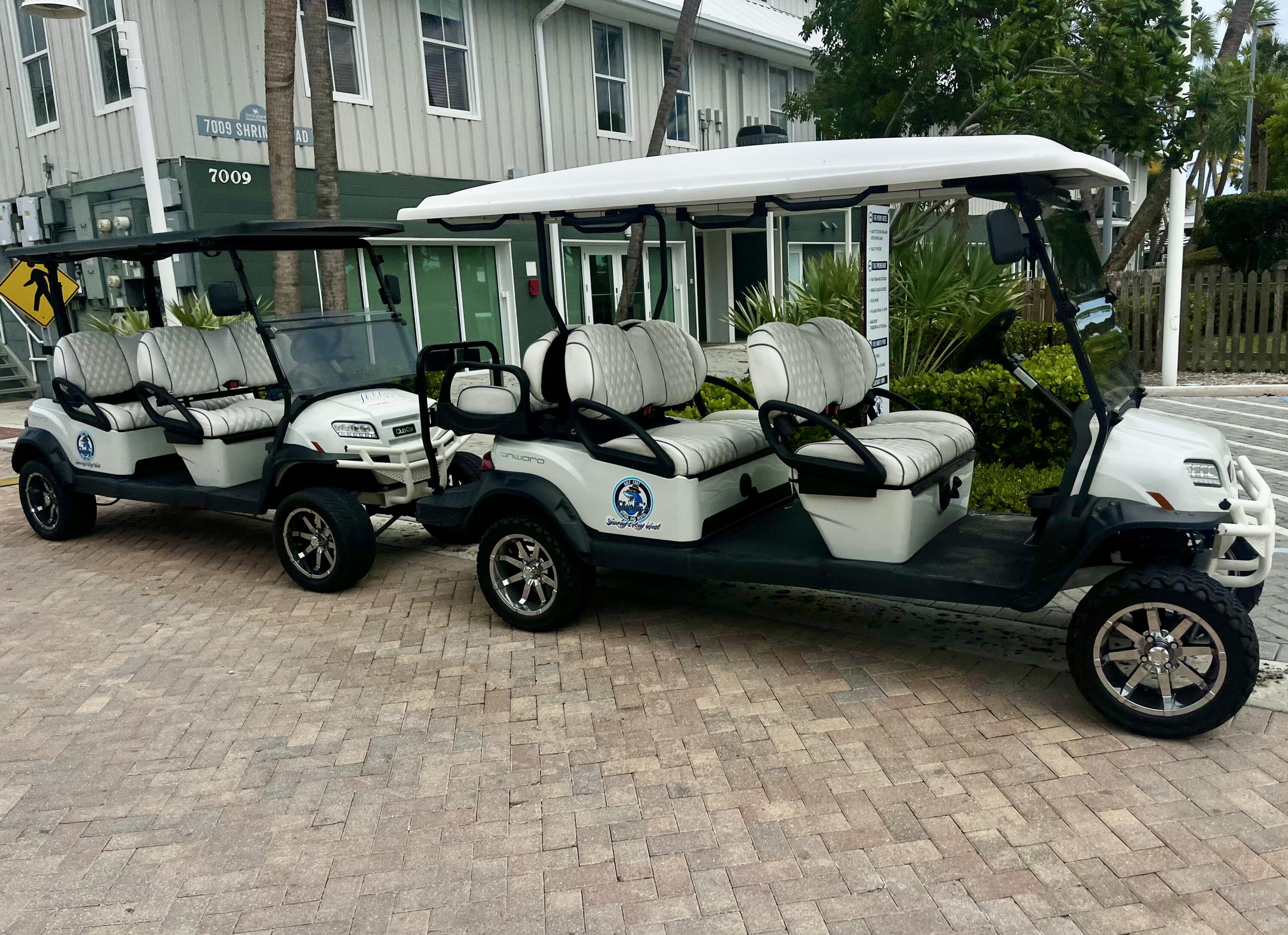 Two white multi-row golf carts parked outside a commercial building.