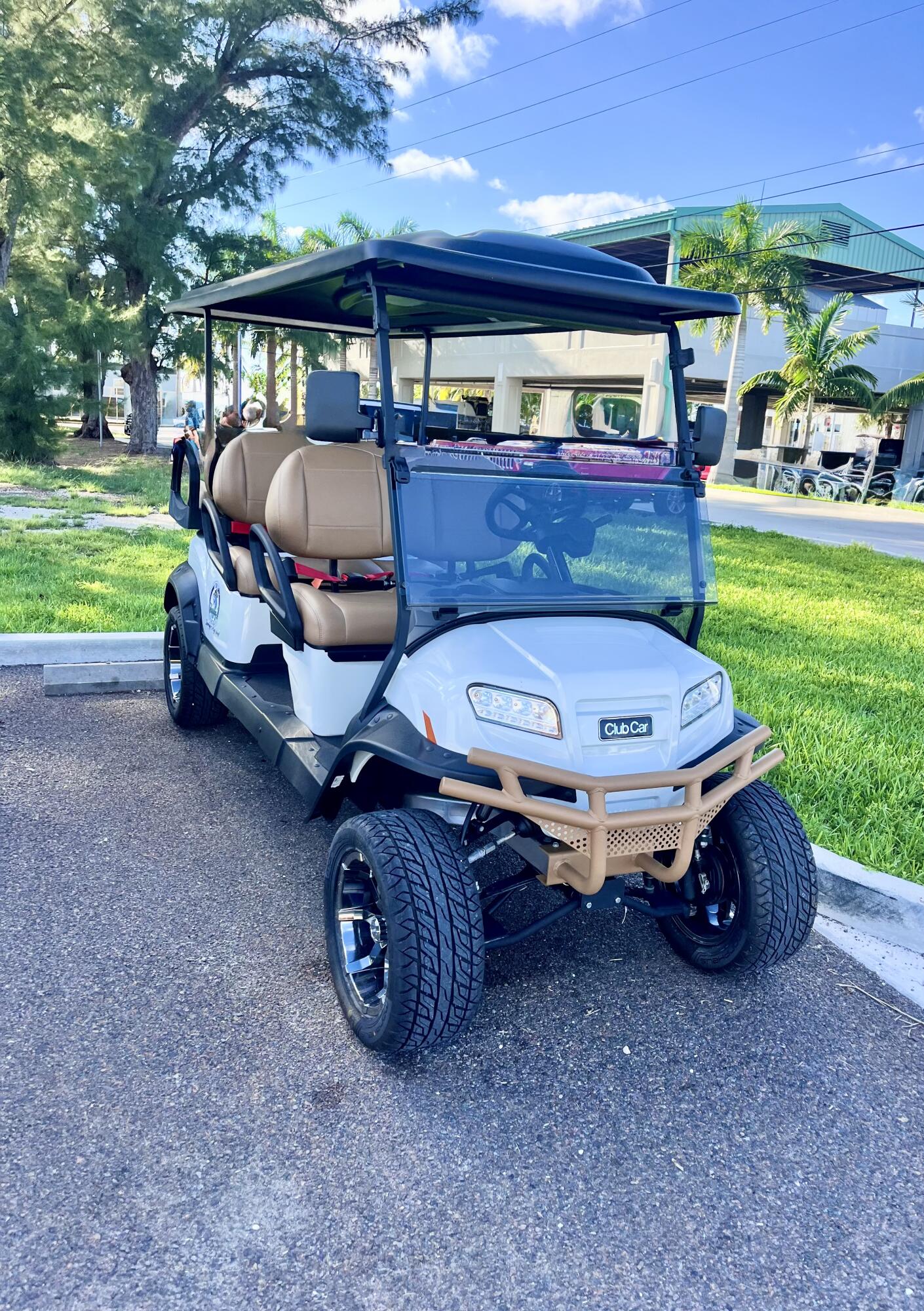 White Club Car golf cart with tan seats, large tires, and a tan front bumper.