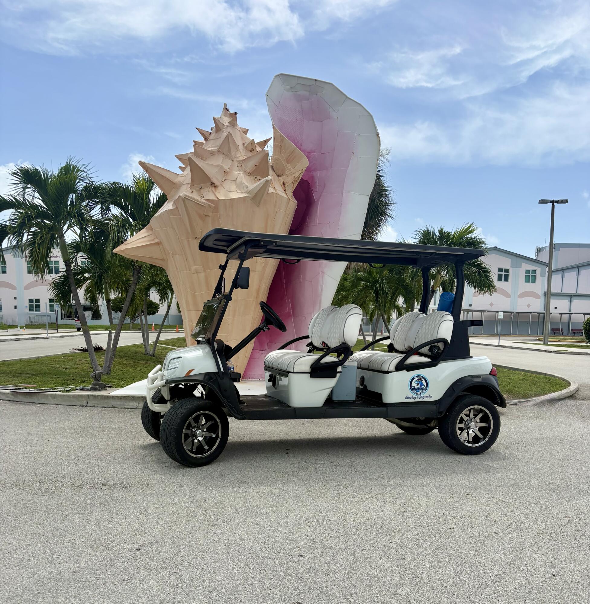 White four-seat golf cart parked beside a large pink shell sculpture.