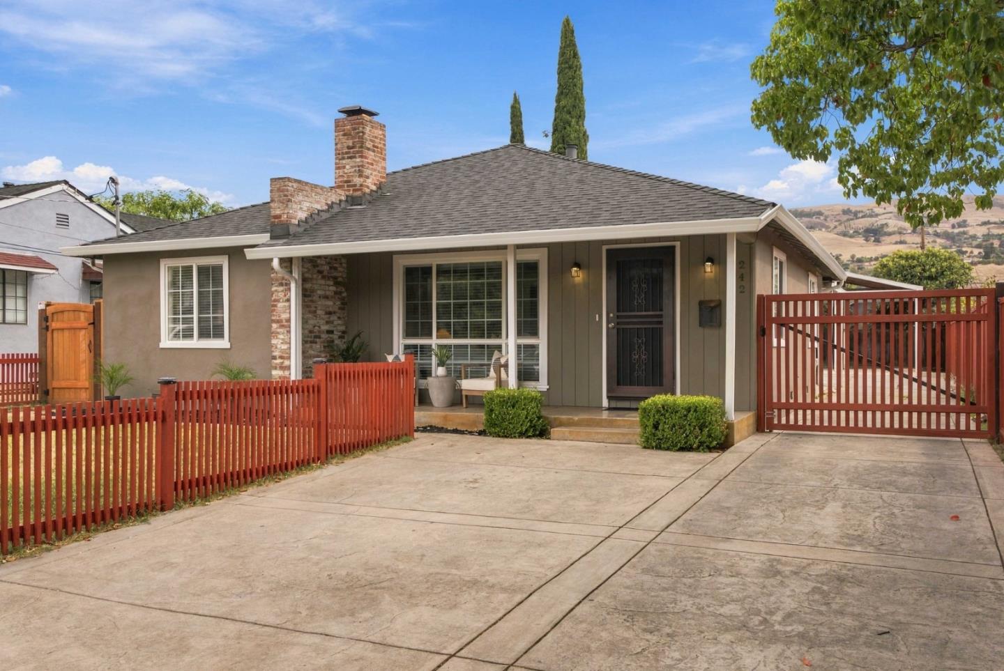 Single-story gray home with a brick chimney, red fencing, and a wide concrete driveway.