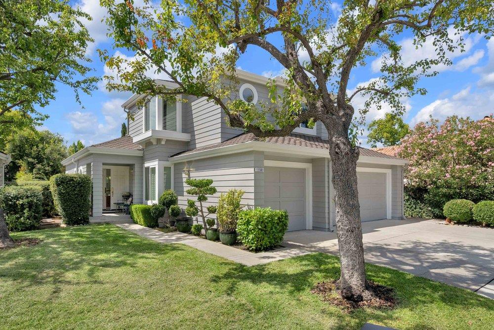 Two-story gray home with two garage doors, landscaped lawn, and a large front-yard tree.
