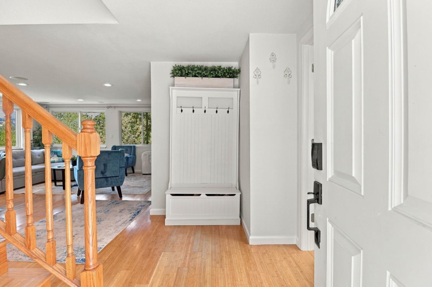 Bright entryway with a white built-in bench, wooden staircase, and blue living room chairs beyond.