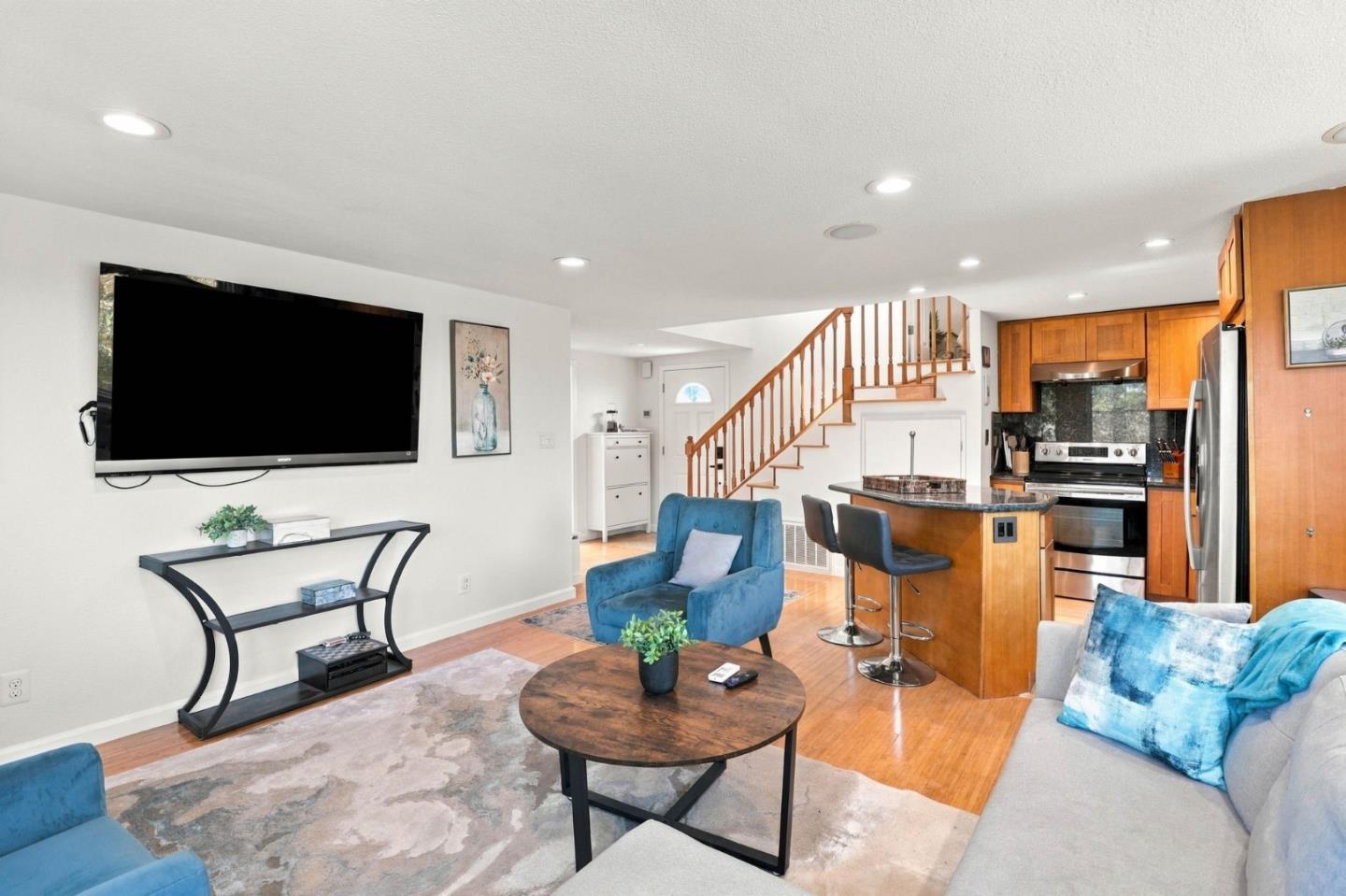 Open-plan living room and kitchen with blue seating, wood cabinetry, and a staircase.