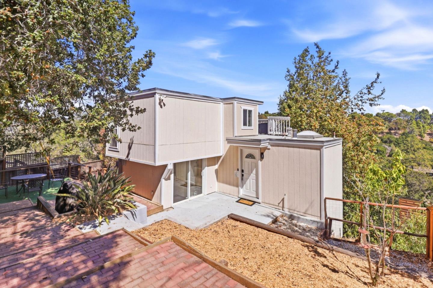 Rear exterior of a beige home with a paved patio and hillside trees.