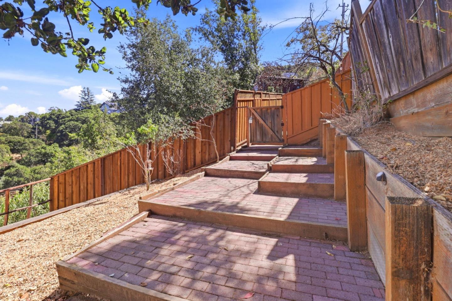 Stepped brick walkway leads to a wooden gate between tall fences and dry landscaping.