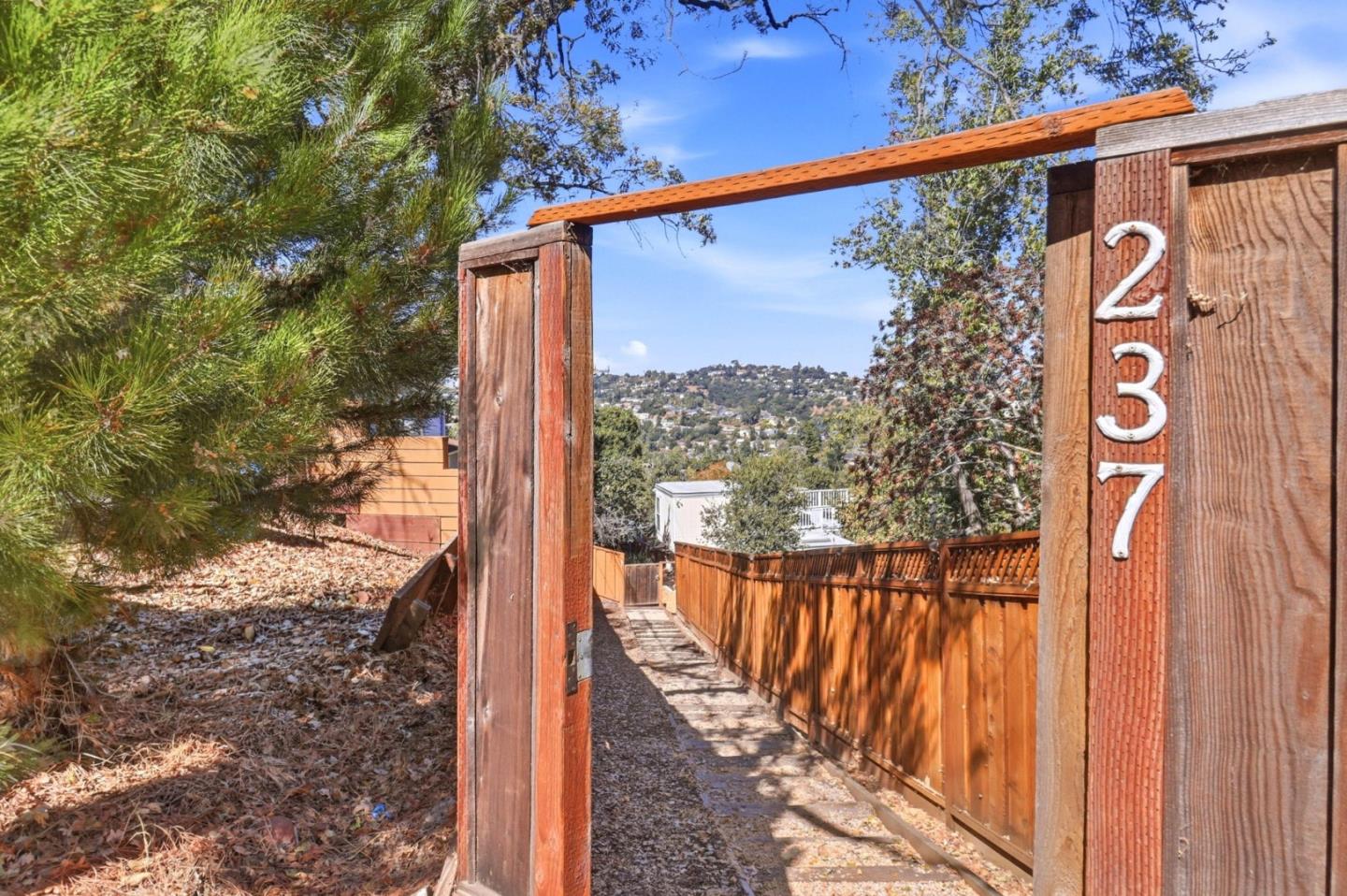 Wooden gate marked 237 opens to a fenced path with a hillside view.