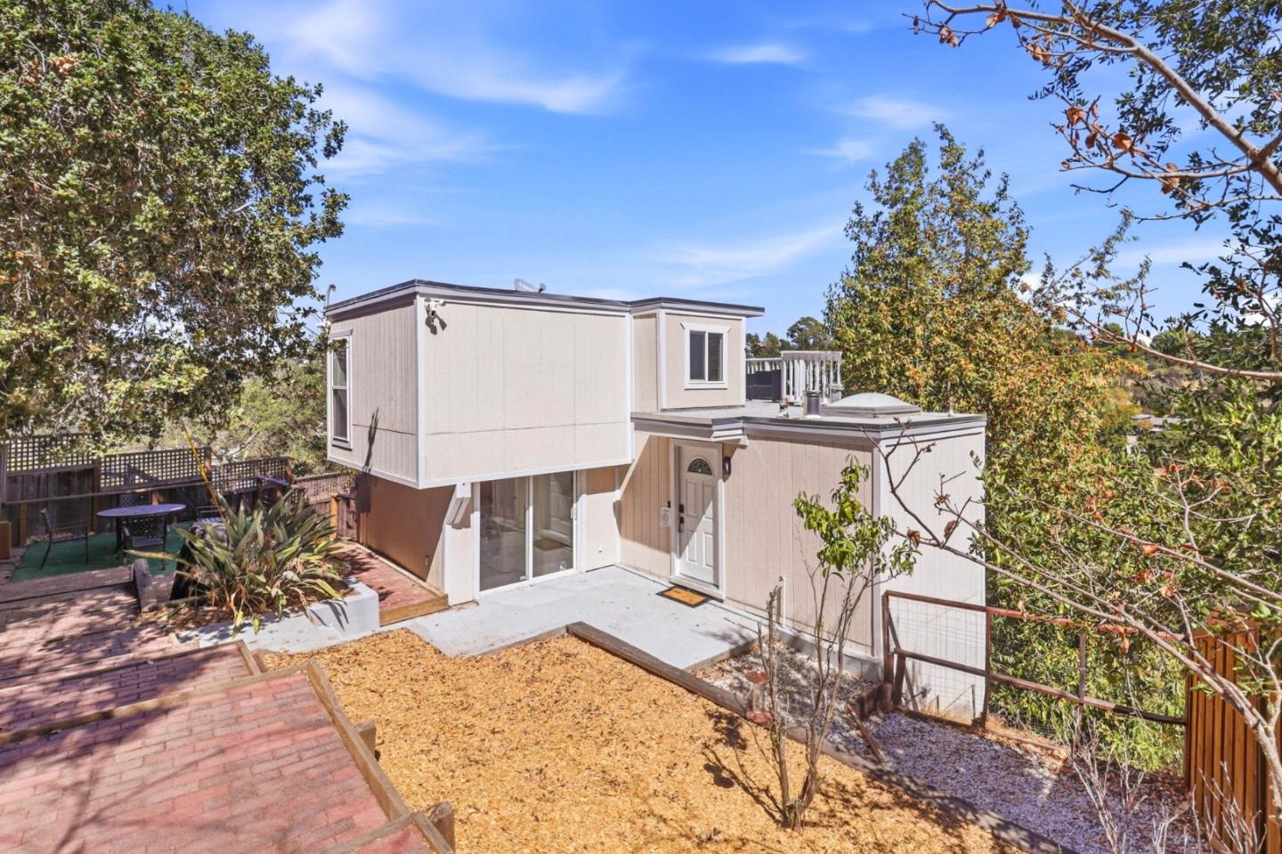 Modern beige home with a flat roof, concrete patio, raised deck, and tree-lined yard.