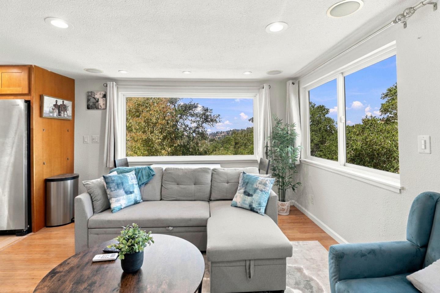 Living room with a gray sectional, teal armchair, and large windows overlooking trees and distant hills.