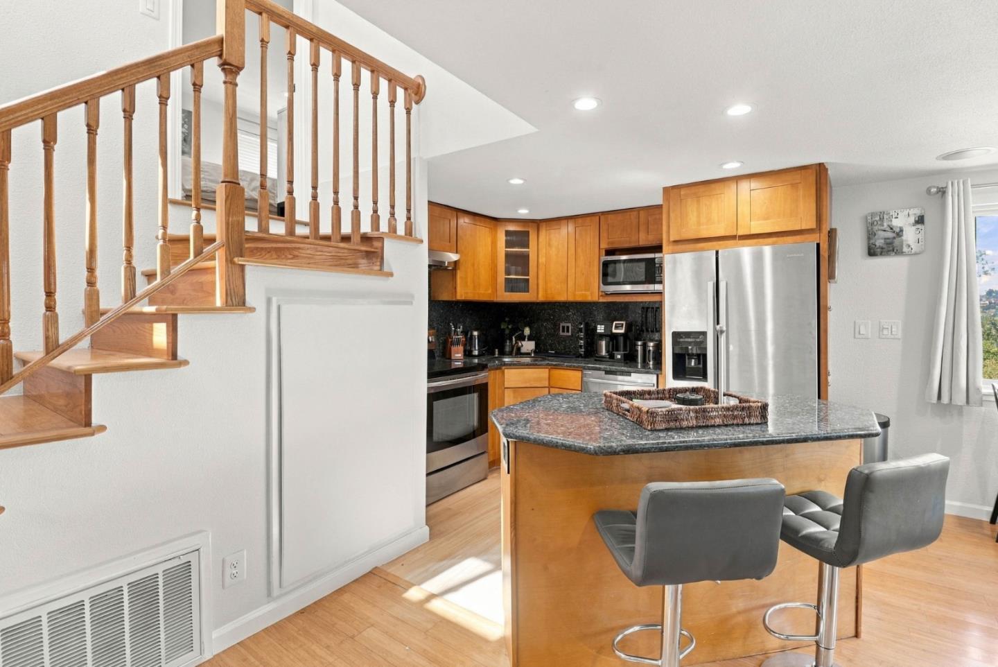 Kitchen with a granite island, warm wood cabinetry, stainless appliances, and a staircase beside it.