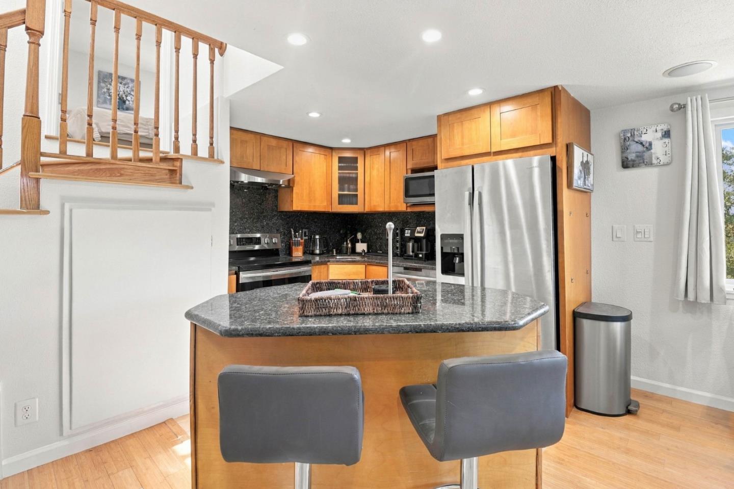 Kitchen with warm wood cabinets, stainless steel appliances, and a stone-topped island with two stools.
