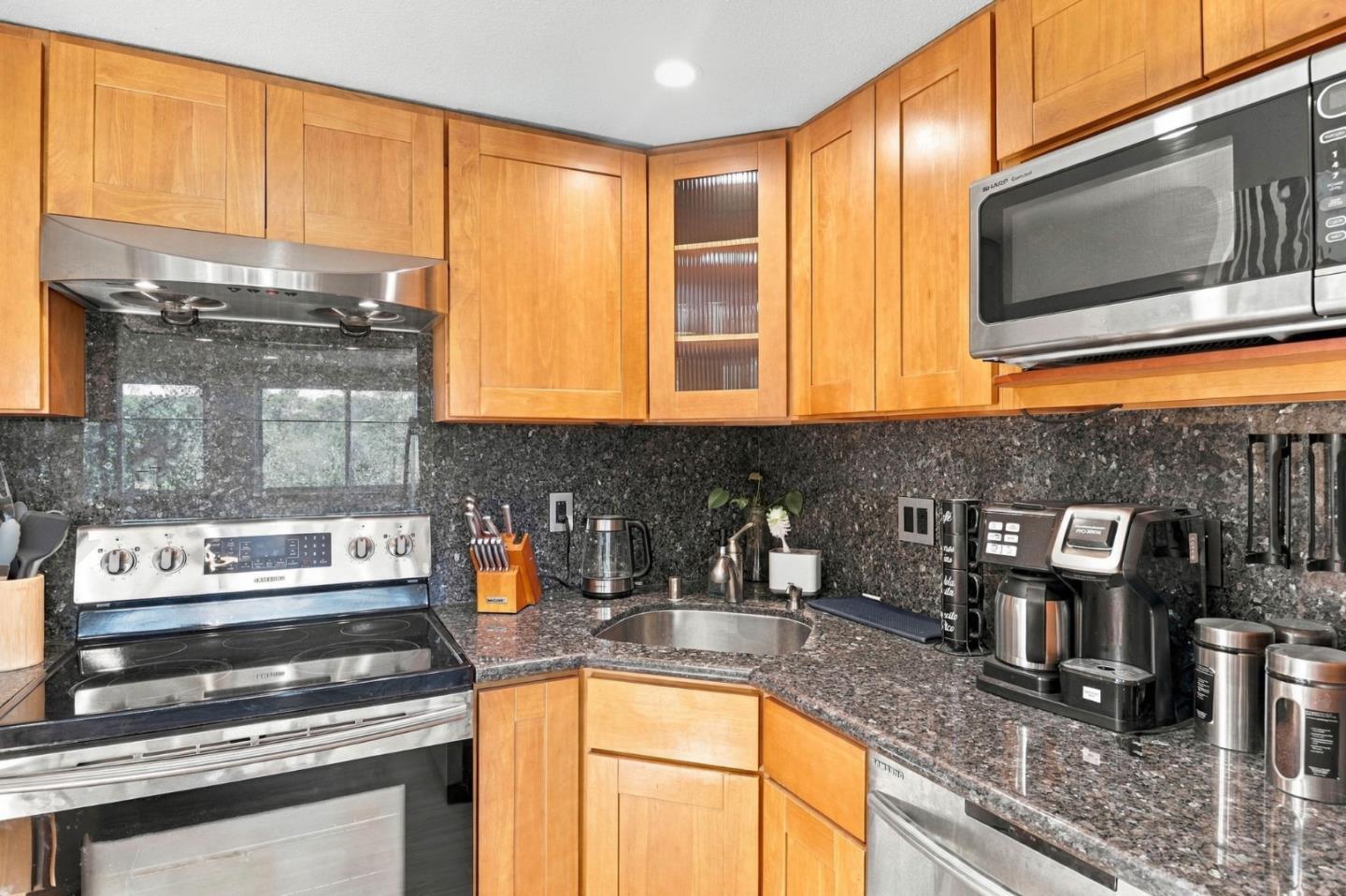 Kitchen with honey-toned wood cabinets, dark stone counters, stainless appliances, and a corner sink.