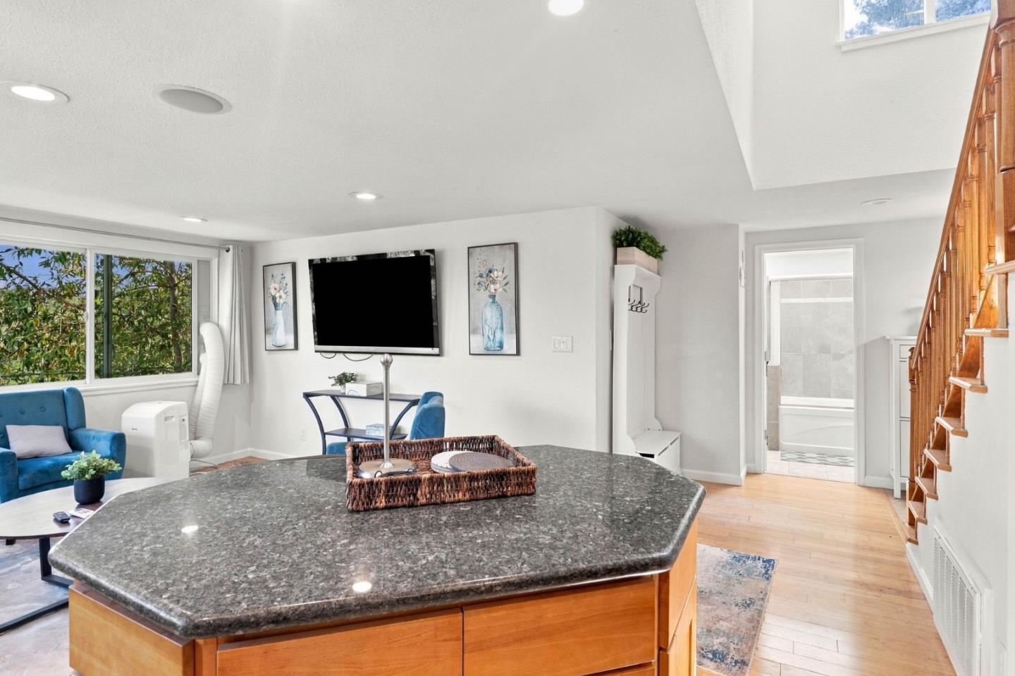 Open-plan kitchen with a large granite island, blue seating, and a wooden staircase.